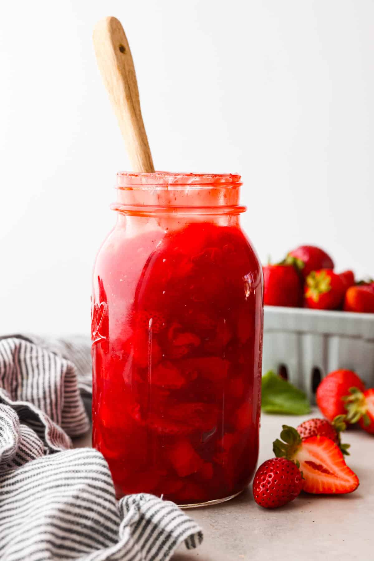 This strawberry pie filling recipe is perfect for anyone who loves a sweet and tangy treat. With easy-to-follow steps and simple ingredients, you'll have a quart of delicious filling ready to enjoy in no time. A jar of strawberry pie filling with a wooden spoon in it.