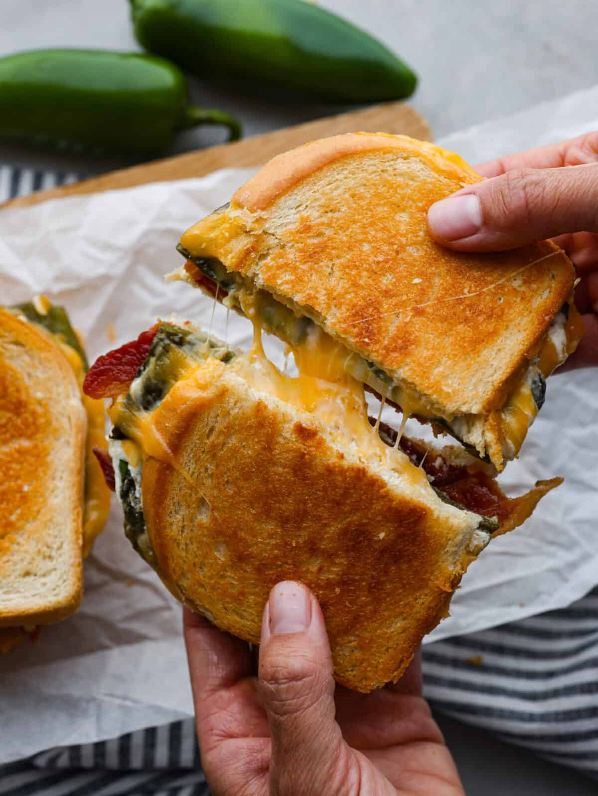 Add some kick to a classic comfort meal with this insanely good jalapeno popper grilled cheese! It's filled with melty colby jack, bacon, spicy jalapeños, and cream cheese to balance the heat and add creaminess. You're going to love it! Two halves of a jalapeno grilled cheese being pulled apart.