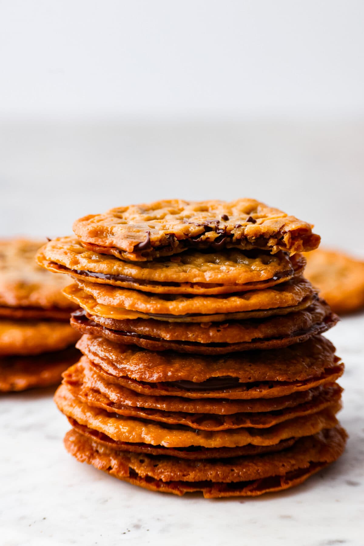 It doesn't get much better than crispy, caramelized cookies with a melted chocolate filling! These lace cookies are super easy to make and just what you need to satisfy your sweet tooth. 8 cookies stacked on top of each other. The top cookie has a bite taken out of it.