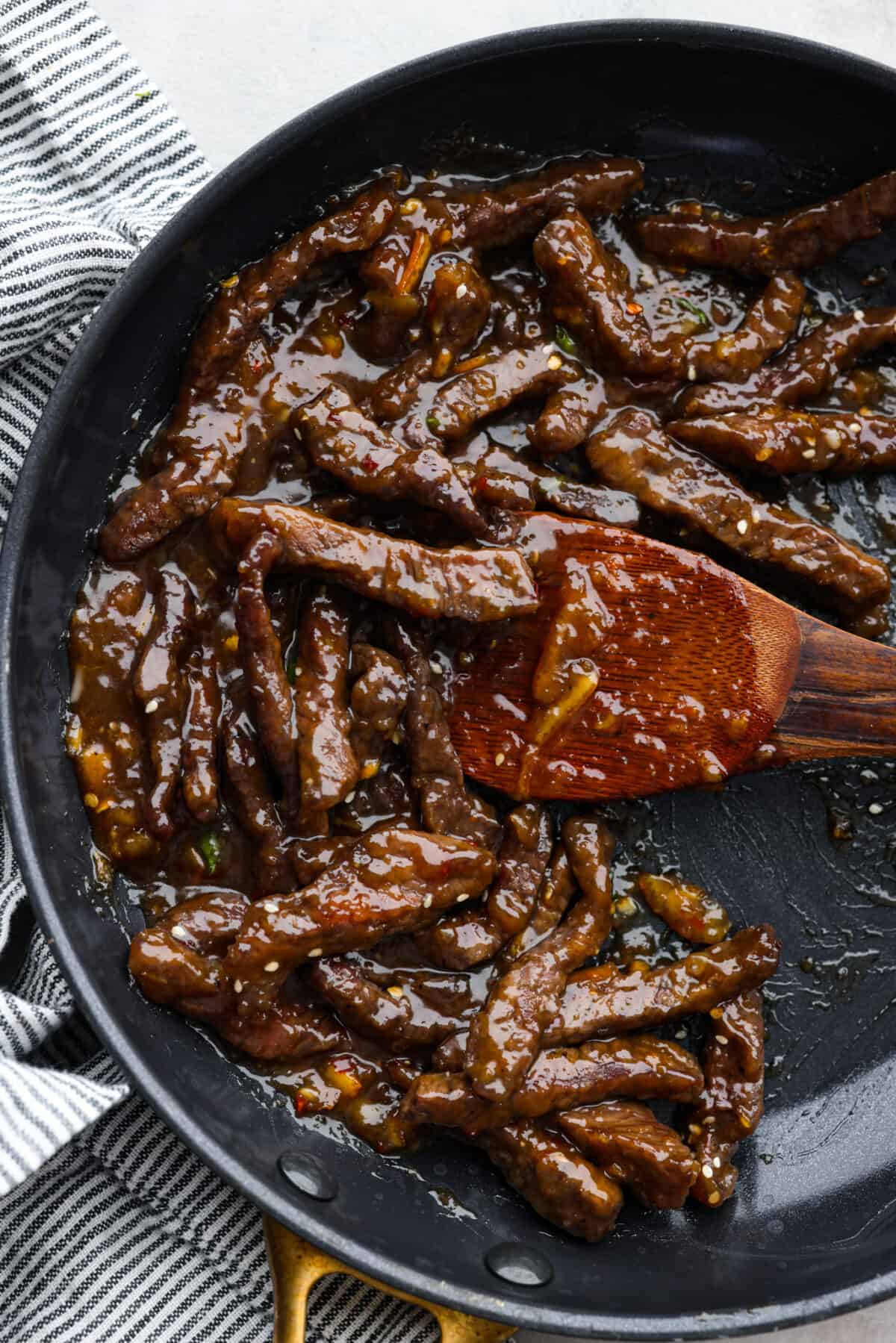 Crispy on the outside, tender on the inside beef strips coated in a tangy orange glaze. This orange beef recipe is the perfect weeknight dinner and sure to become a new family favorite! It may even rival your favorite takeout spot. Top-down view of orange beef in a skillet, being stirred with a wooden spoon.