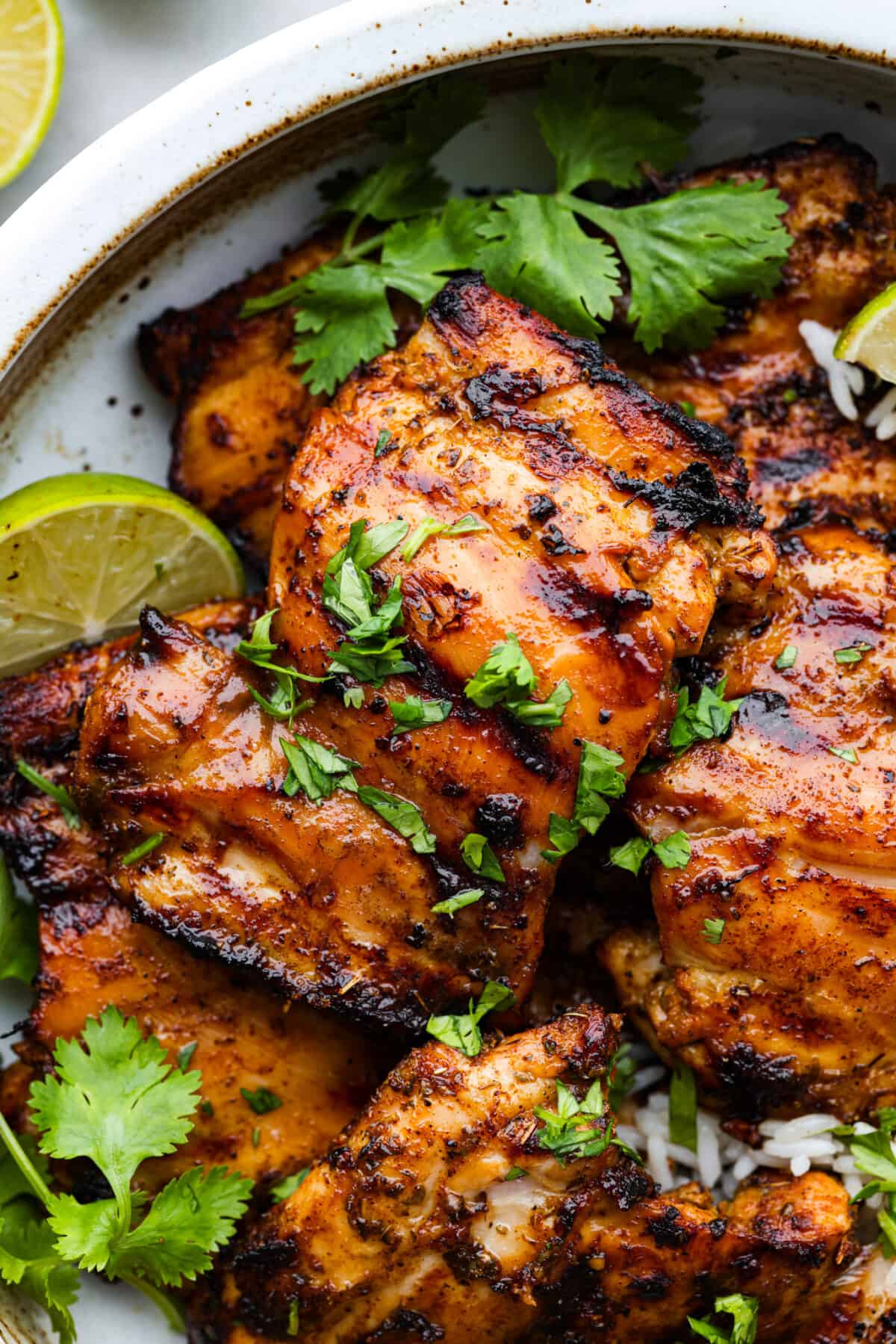 Mexican pollo asado is some of the juiciest, most flavorful grilled chicken you'll ever taste. Each chicken thigh is marinated in a mix of tangy lime, orange, and a blend of spices for some kick. You'll love each tender, flavor-packed bite! Closeup of pollo asado, garnished with herbs.
