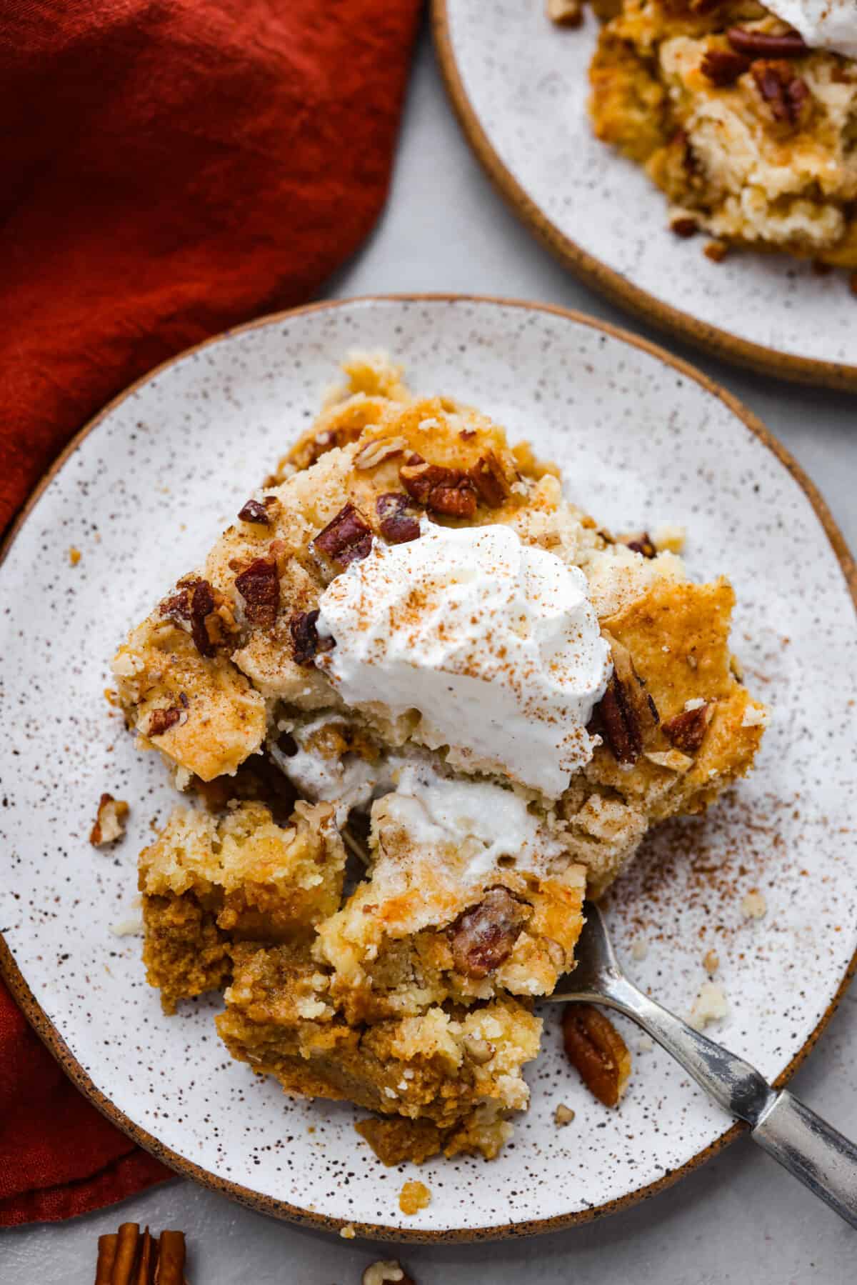 This pumpkin dump cake is a delicious fall favorite that combines the rich flavors of pumpkin, spices, and a cake mix. It's a mouthwatering treat that's incredibly easy to make! The top view of a slice of pumpkin dump cake on a plate.