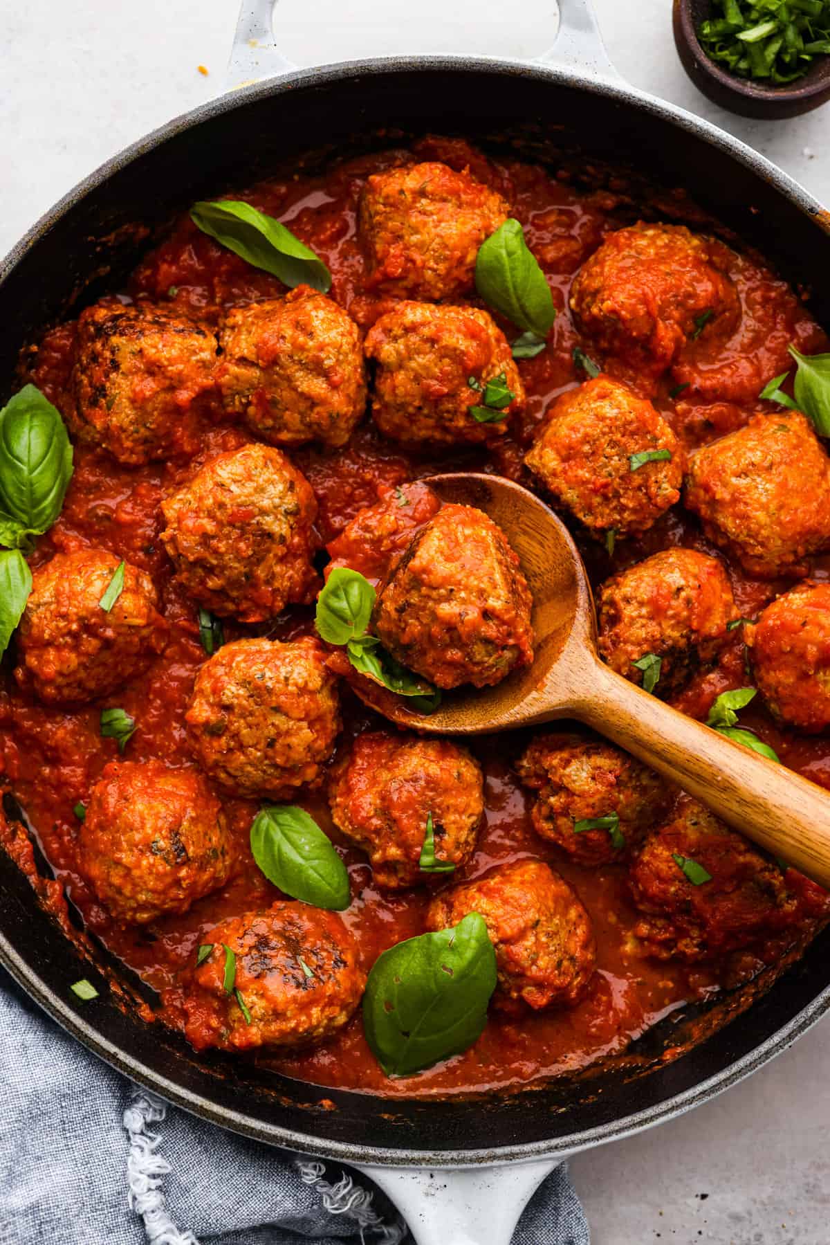 Level up your meatball game with the addition of ricotta cheese! These ricotta meatballs have the creamiest texture and turn out extra tender and juicy. The flavors are incredible and your family will beg you to make these every week! Top view of ricotta meatballs and marinara sauce in a black skillet. A wooden spoon is lifting up a meatball.
