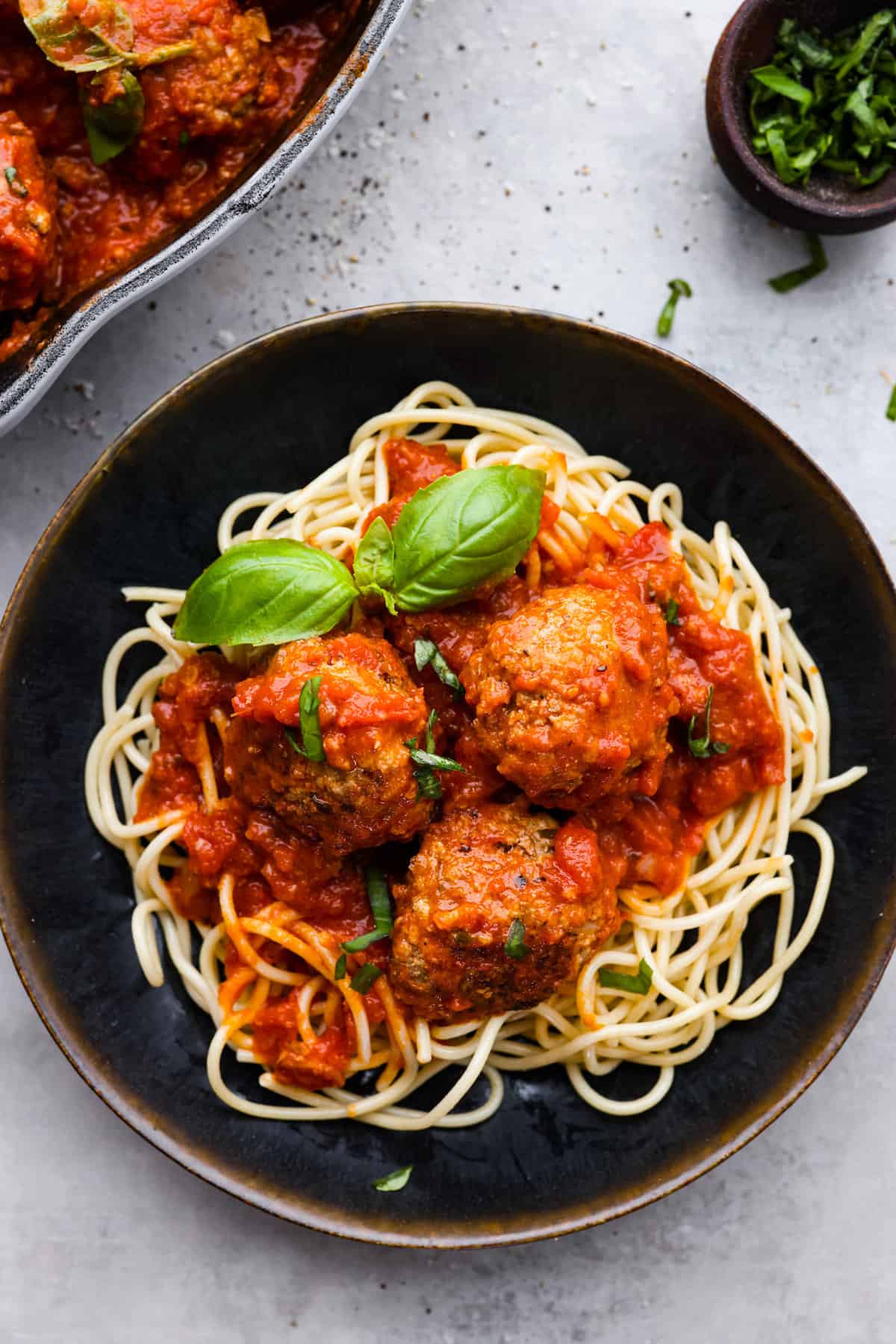 Level up your meatball game with the addition of ricotta cheese! These ricotta meatballs have the creamiest texture and turn out extra tender and juicy. The flavors are incredible and your family will beg you to make these every week! Top view of ricotta meatballs on a bed of spaghetti noodles in a black bowl.