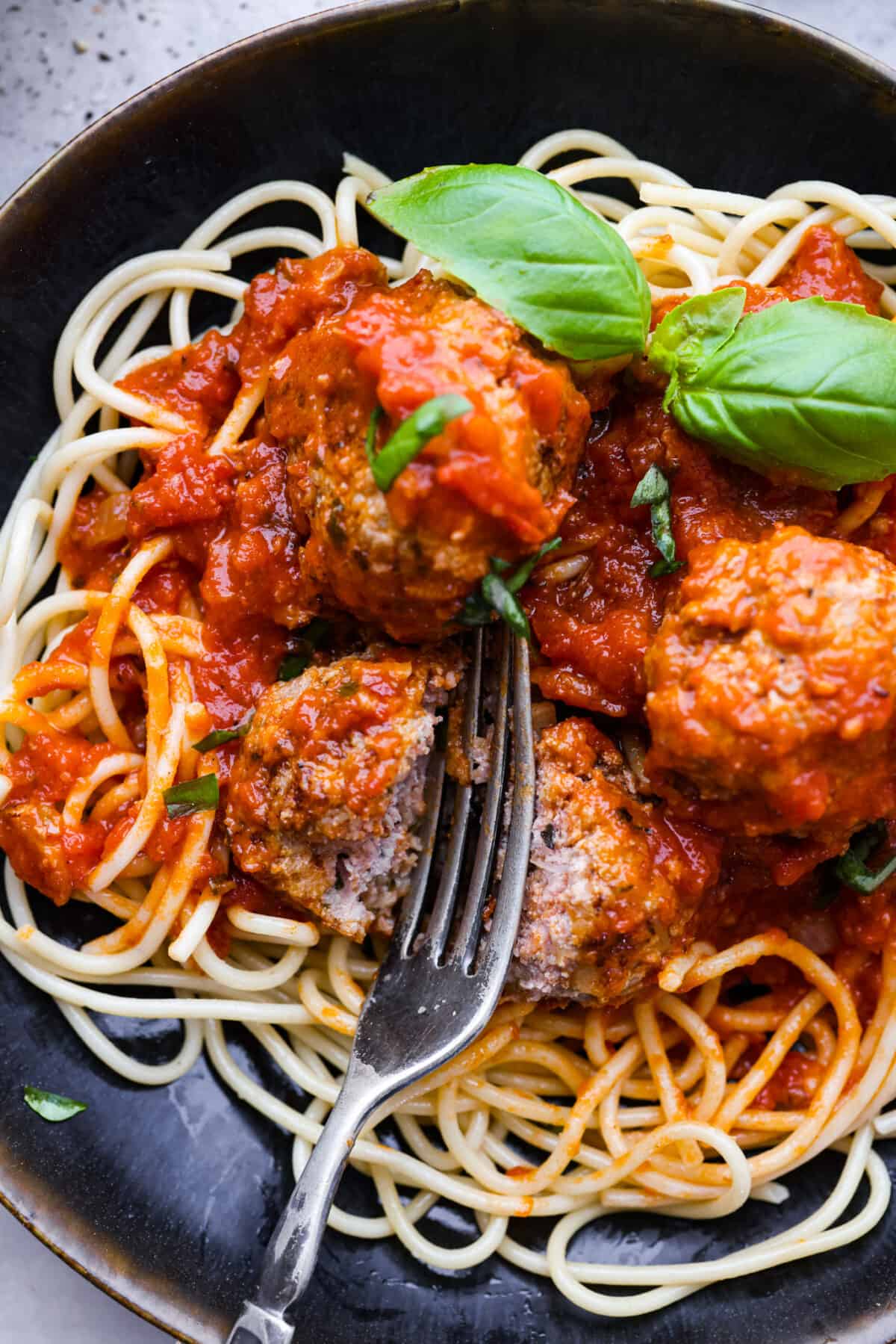 Level up your meatball game with the addition of ricotta cheese! These ricotta meatballs have the creamiest texture and turn out extra tender and juicy. The flavors are incredible and your family will beg you to make these every week! Close view of a fork cutting into a meatball with marinara and noodles.