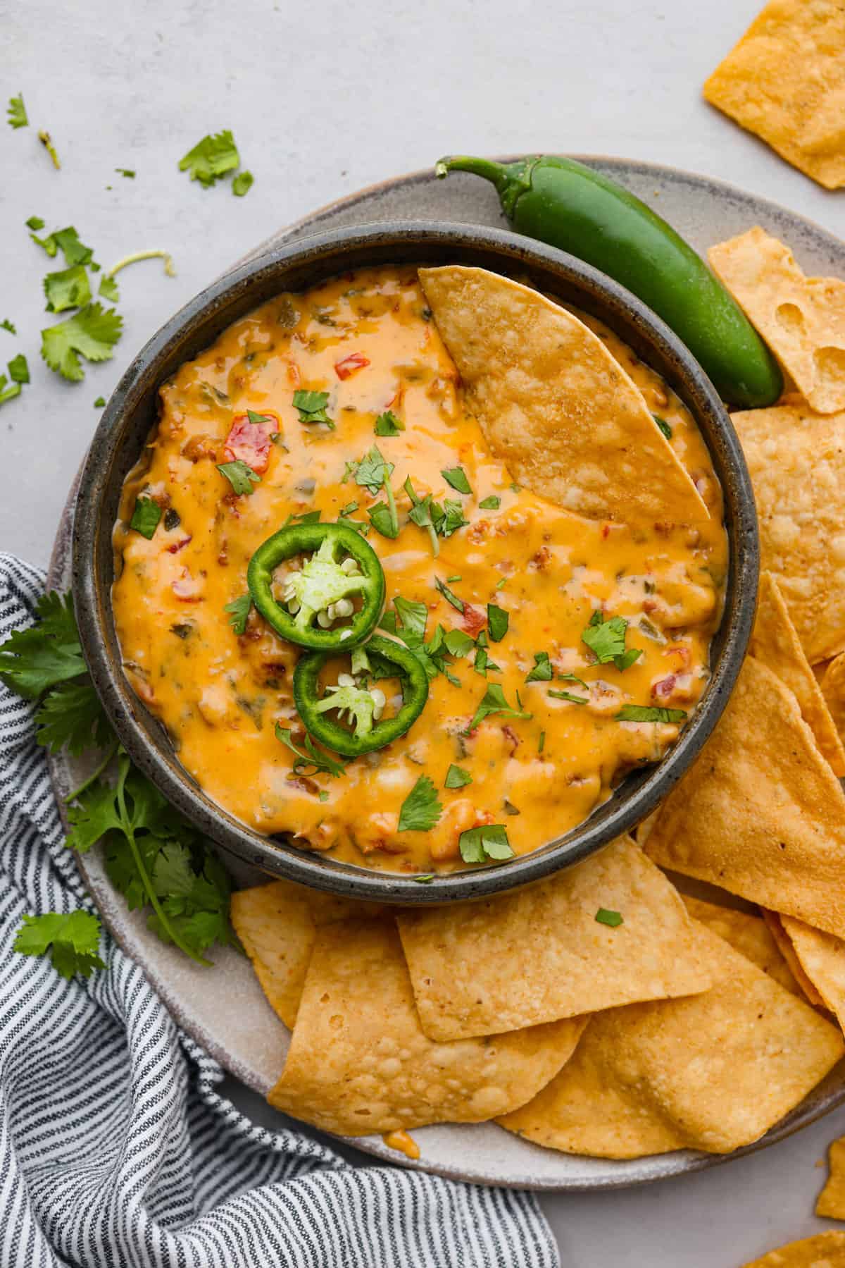 Bring this easy and flavorful smoked queso dip to your next party or game day! Add the cheeses chorizo, Rotel, cilantro, garlic, onion, and salsa verde all into the same pan, then let the Traeger do the rest. You'll love the hint of smokiness that enhances the Mexican flavors in this dip. Top view of smoked queso dip in a black bowl on top of a serving platter. Chips and cilantro surround the bowl with a chip resting in the dip.