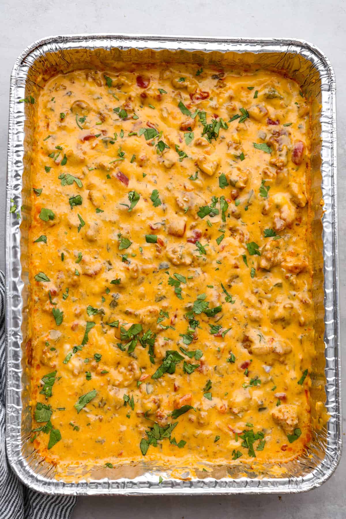 Bring this easy and flavorful smoked queso dip to your next party or game day! Add the cheeses chorizo, Rotel, cilantro, garlic, onion, and salsa verde all into the same pan, then let the Traeger do the rest. You'll love the hint of smokiness that enhances the Mexican flavors in this dip. Top view of smoked queso dip in a disposable aluminum pan.