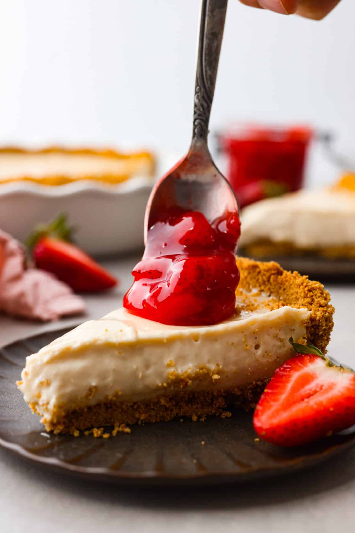 This strawberry pie filling recipe is perfect for anyone who loves a sweet and tangy treat. With easy-to-follow steps and simple ingredients, you'll have a quart of delicious filling ready to enjoy in no time. Strawberry pie filling being dolloped onto a piece of cheesecake.