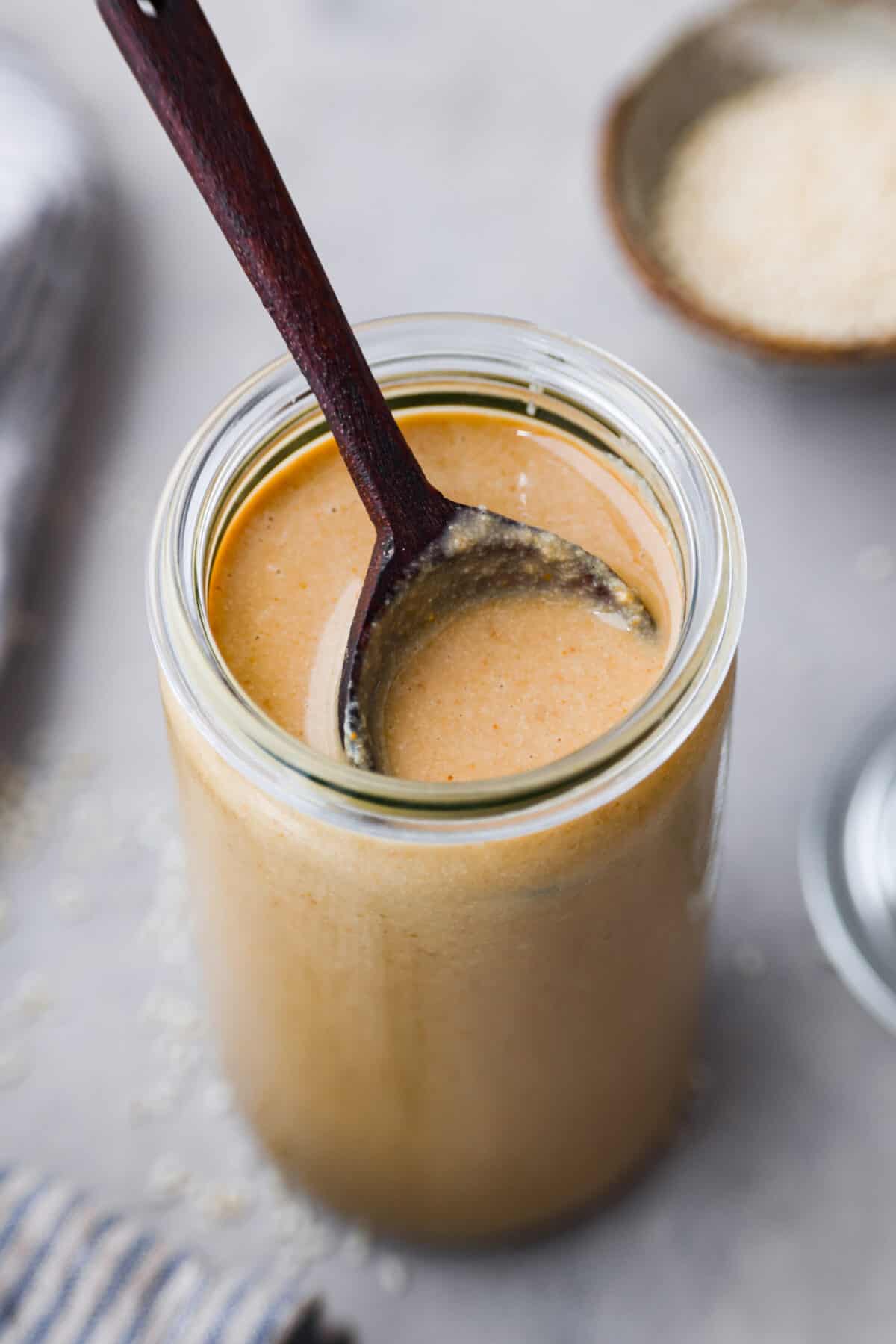 Make this easy tahini right at home with just sesame seeds and olive oil. This Middle Eastern condiment resembles the same texture as nut butter and is a staple ingredient used in sauces, savory dishes, and even desserts! Close view of a wood spoon set inside a glass jar of tahini.