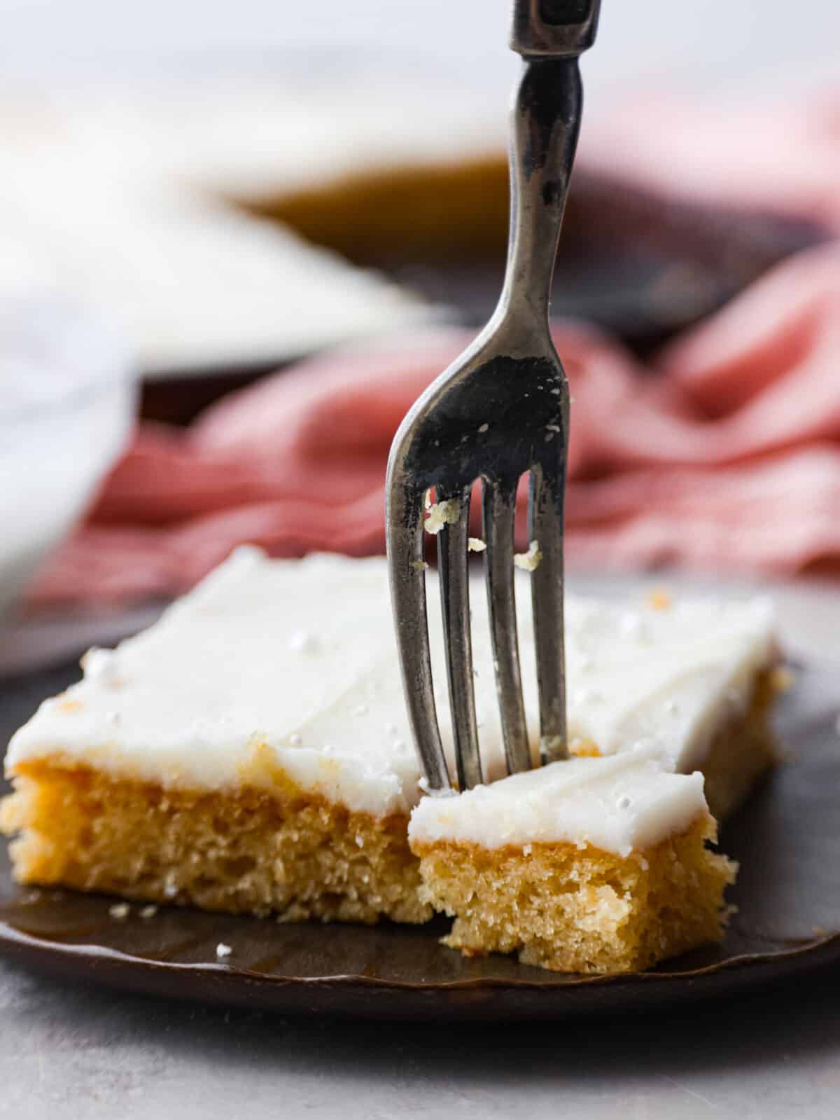 Not only does this white Texas sheet cake feed a crowd, but it's always a hit with its buttery, almond flavor. Topped off with a smooth layer of buttercream frosting, you'll be going back for slice after slice! Closeup of a slice of cake, with a bite being taken out of it.