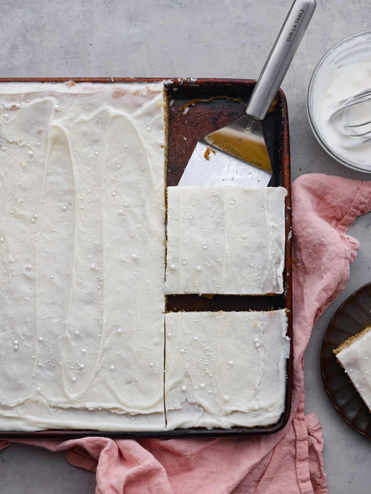 Not only does this white Texas sheet cake feed a crowd, but it's always a hit with its buttery, almond flavor. Topped off with a smooth layer of buttercream frosting, you'll be going back for slice after slice! Top-down view of the Texas sheet cake, cut into squares.