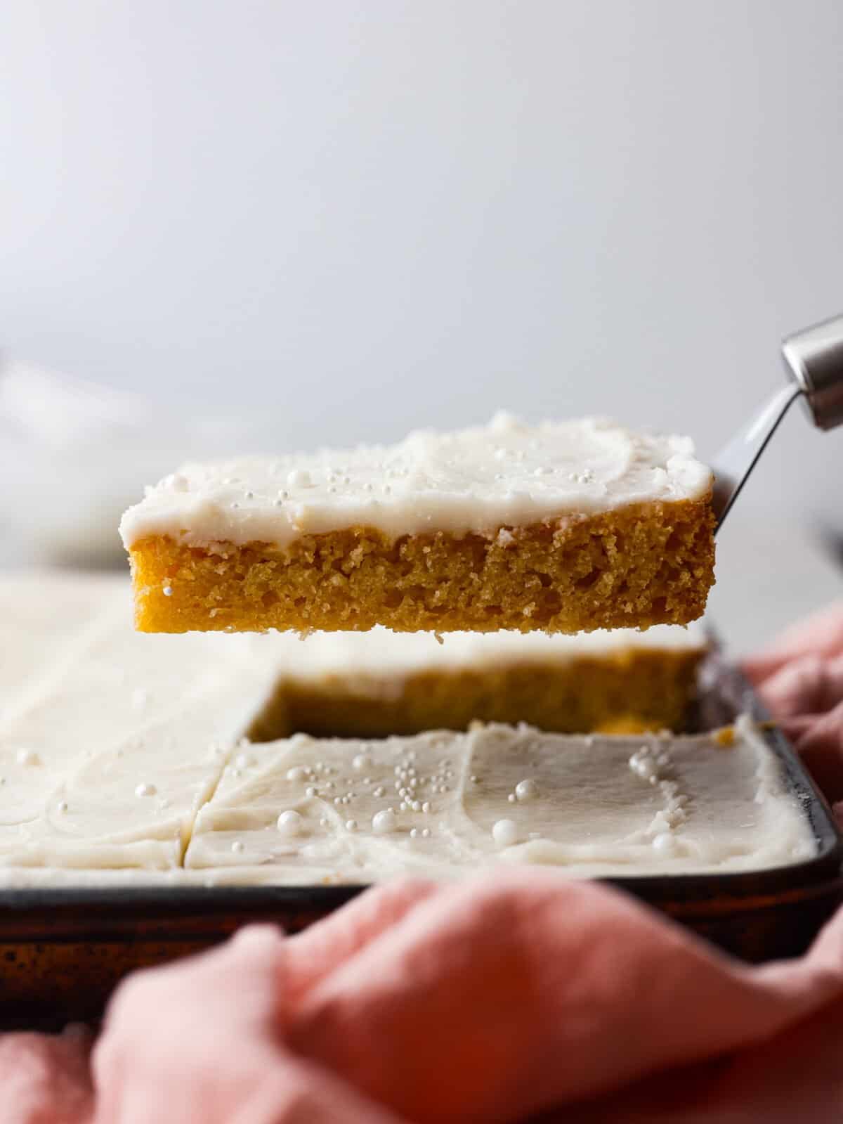 Not only does this white Texas sheet cake feed a crowd, but it's always a hit with its buttery, almond flavor. Topped off with a smooth layer of buttercream frosting, you'll be going back for slice after slice! Serving a slice of white Texas sheet cake.