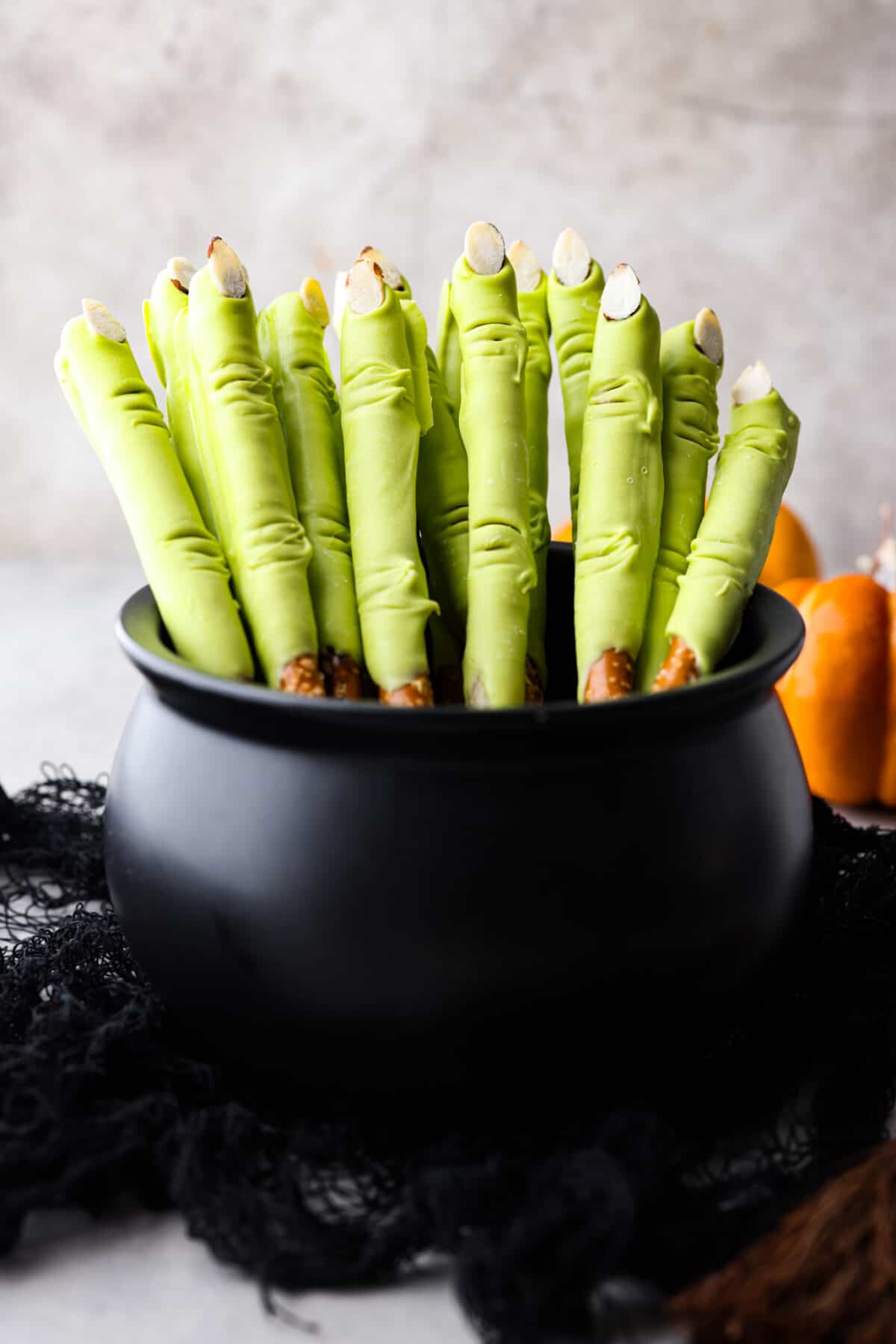 Get ready for a spooky Halloween delight with these Witch Fingers! A classic twist on pretzel rods, this bewitching treat is dipped in green candy melts and decorated with almond nails and knuckles. It makes for a fun and easy treat that's perfect for the season. A black cauldron filed with witch fingers.