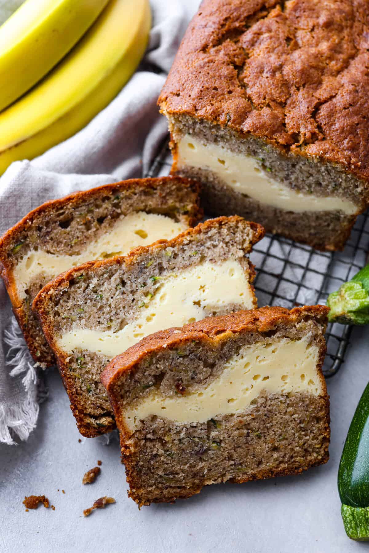 Overripe bananas and zucchini get used in this delicious and perfectly moist bread. The cream cheese swirl hidden inside is the best part! Enjoy a slice of cream cheese banana zucchini bread fresh out of the oven and thank me later. Hero image of 3 slices of bread.