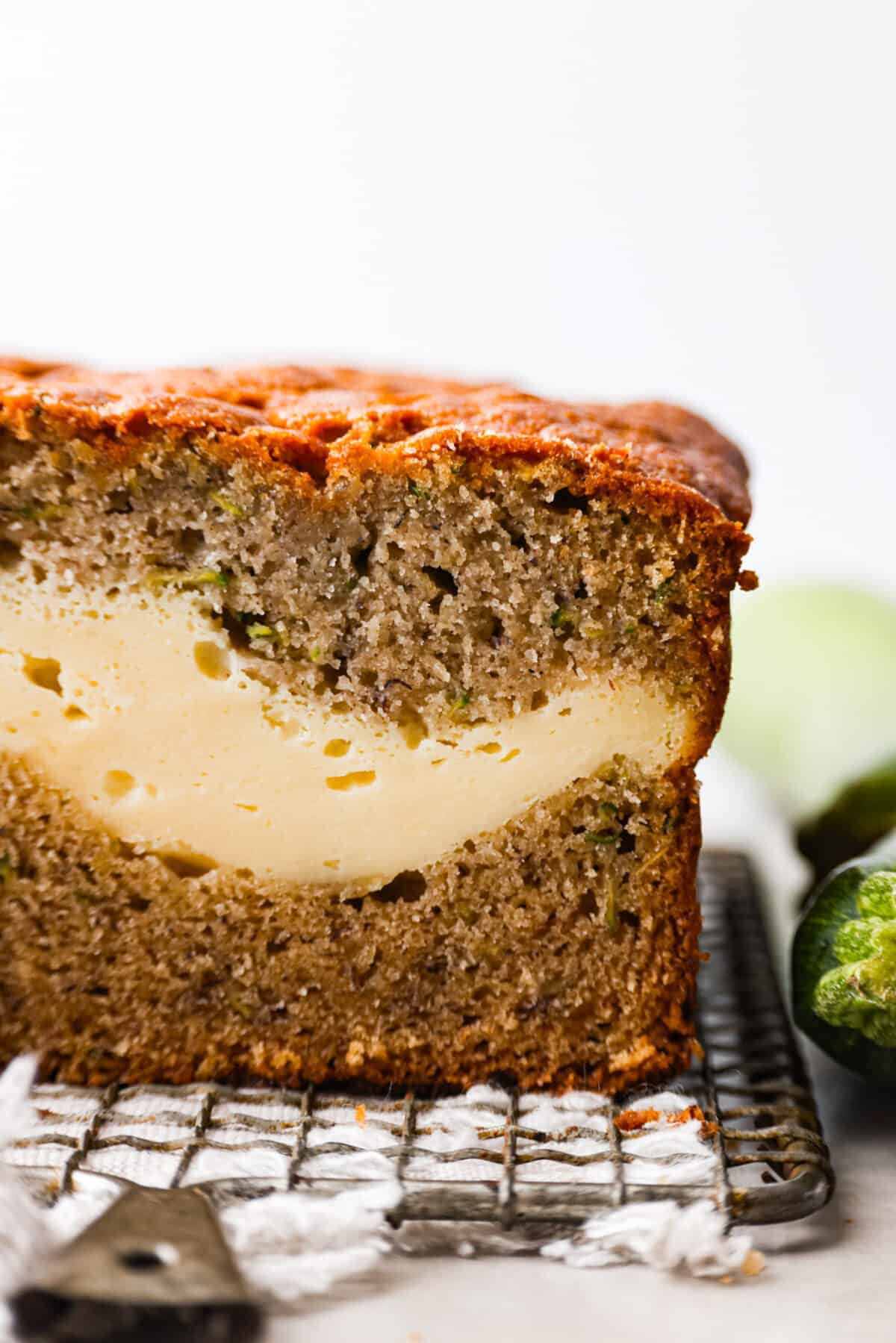 Overripe bananas and zucchini get used in this delicious and perfectly moist bread. The cream cheese swirl hidden inside is the best part! Enjoy a slice of cream cheese banana zucchini bread fresh out of the oven and thank me later. Closeup of a slice of cream cheese banana zucchini bread.