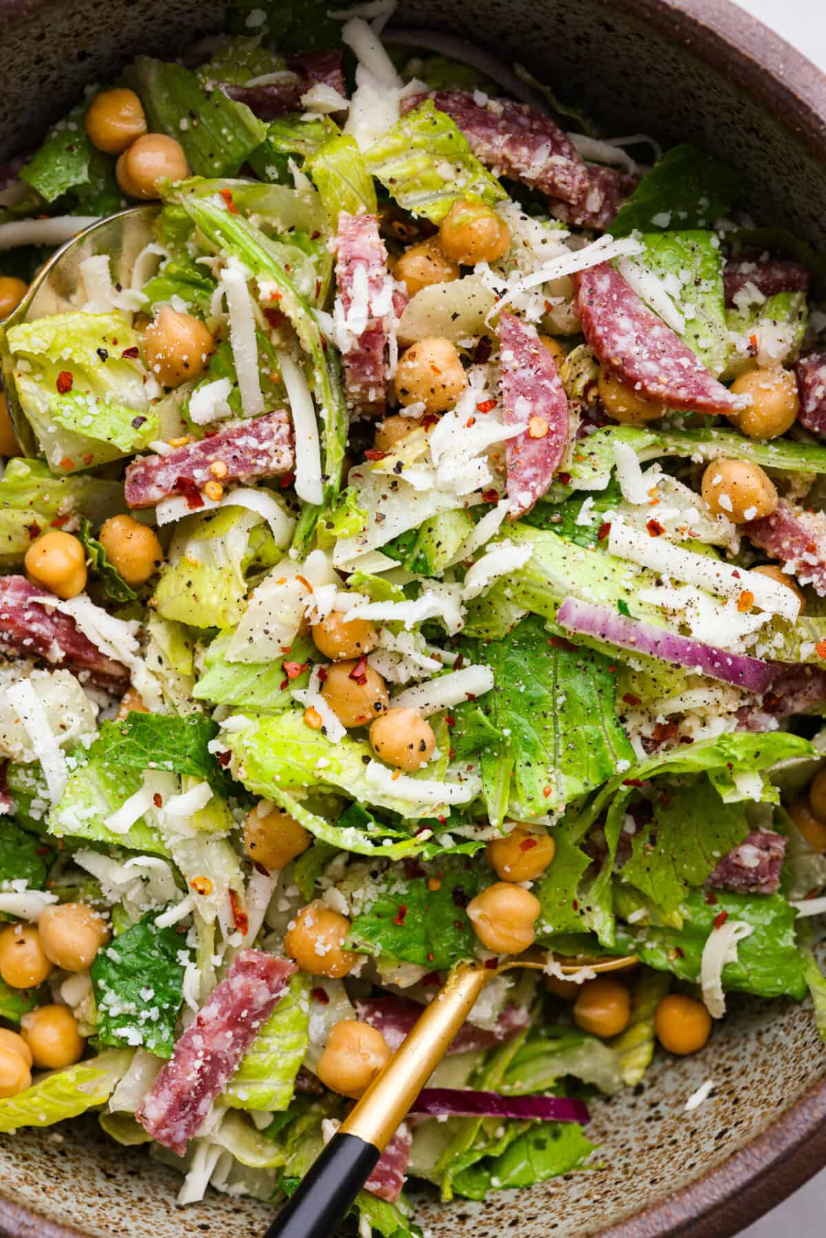 Fresh and flavorful, La Scala Salad is a copycat recipe of the famous Italian chopped salad served at La Scala restaurant in Beverly Hills. Rumor has it, Kim Kardashian orders this salad often, and for good reason! It's packed with delicious ingredients and crunchy texture, thanks to the chickpeas, salami, mozzarella cheese, and a zesty red wine vinaigrette. Closeup of salad made with salami, chickpeas, lettuce, and grated cheese.