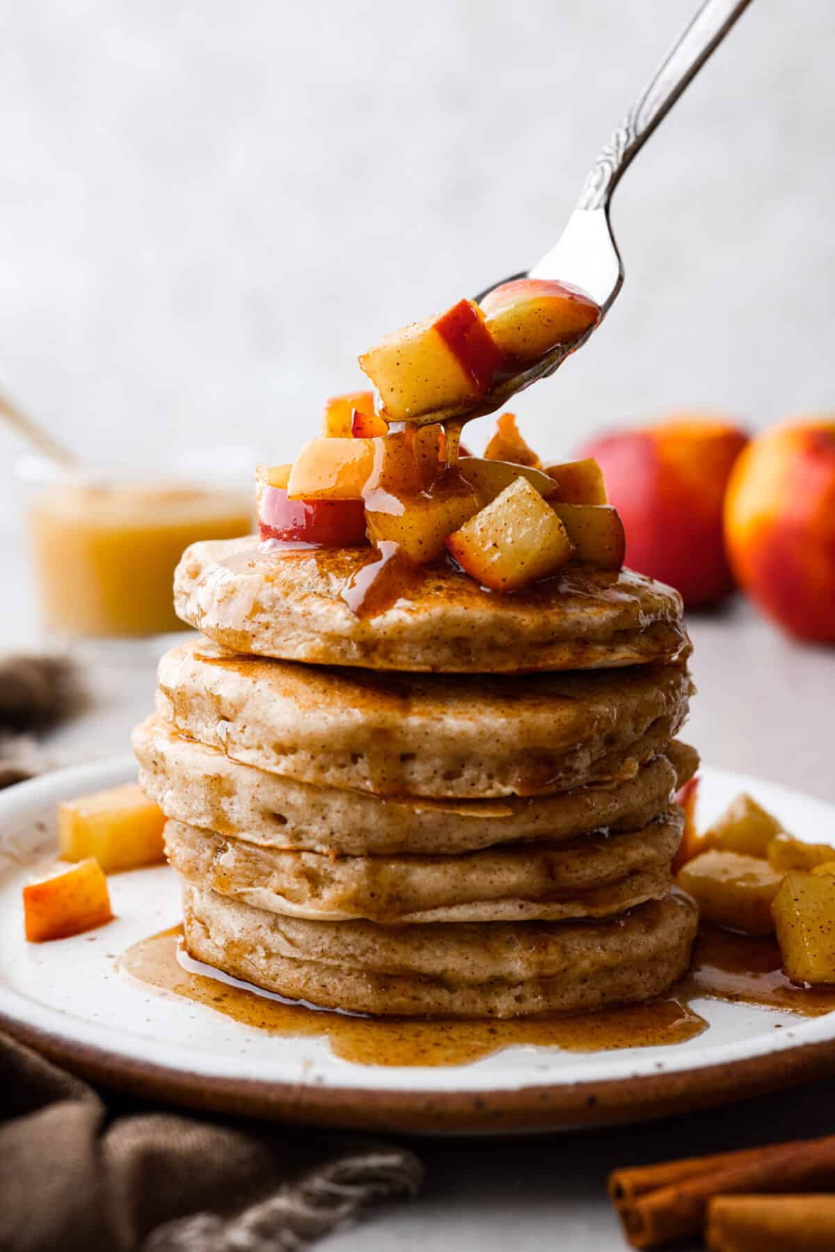 Fluffy applesauce pancakes are easy and delicious with a hint of brown sugar and cinnamon for a cozy fall flavor. The addition of applesauce gives these homemade pancakes the perfect texture. These will quickly become your favorite fall breakfast! Close view of a stack of applesauce pancakes with a spoon placing sauteed apples on top.