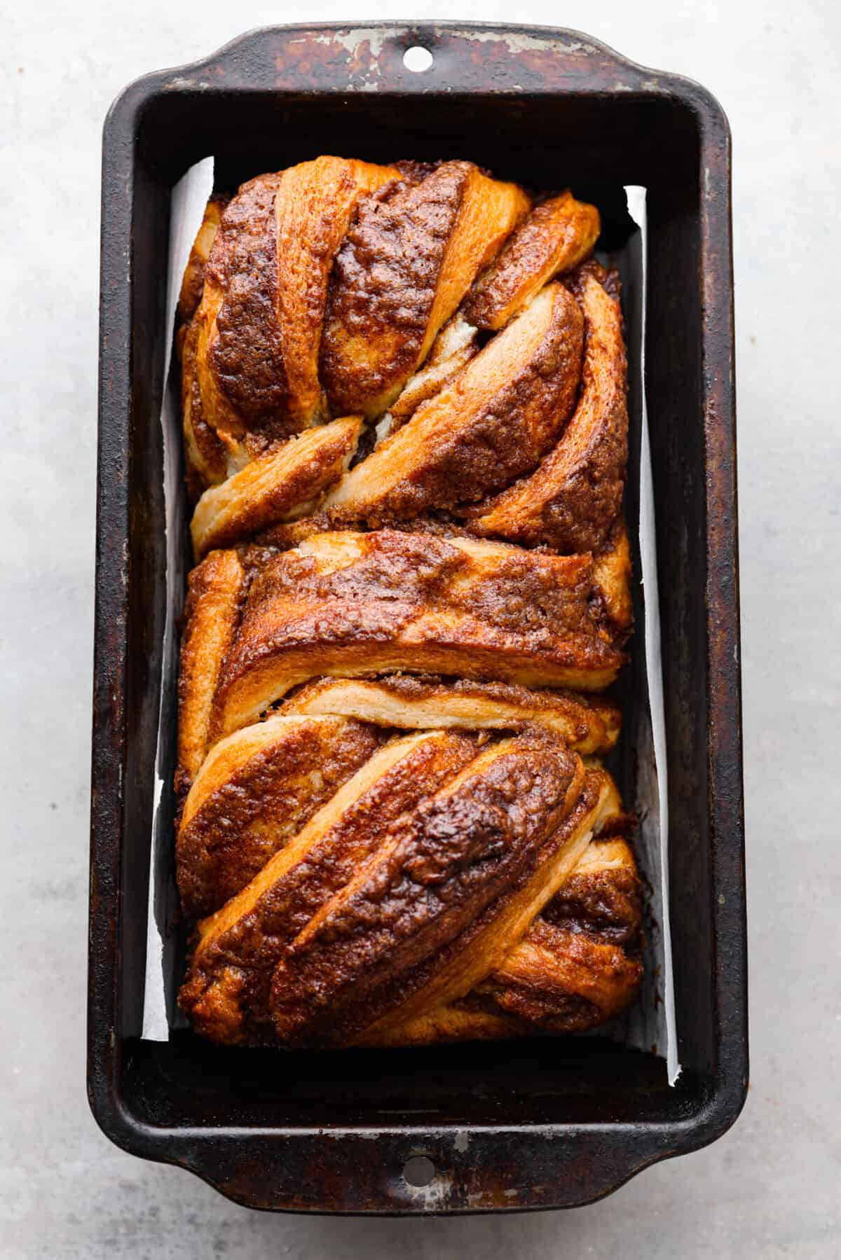 Delicious Cinnamon Babka is rich, buttery bread with swirling ribbons of cinnamon sugar, topped off with aย sweet syrup topping. Tender, soft, and perfectly sweet, this loaf is a welcome treat for any occasion! The top view of cinnamon babka baked in a pan.