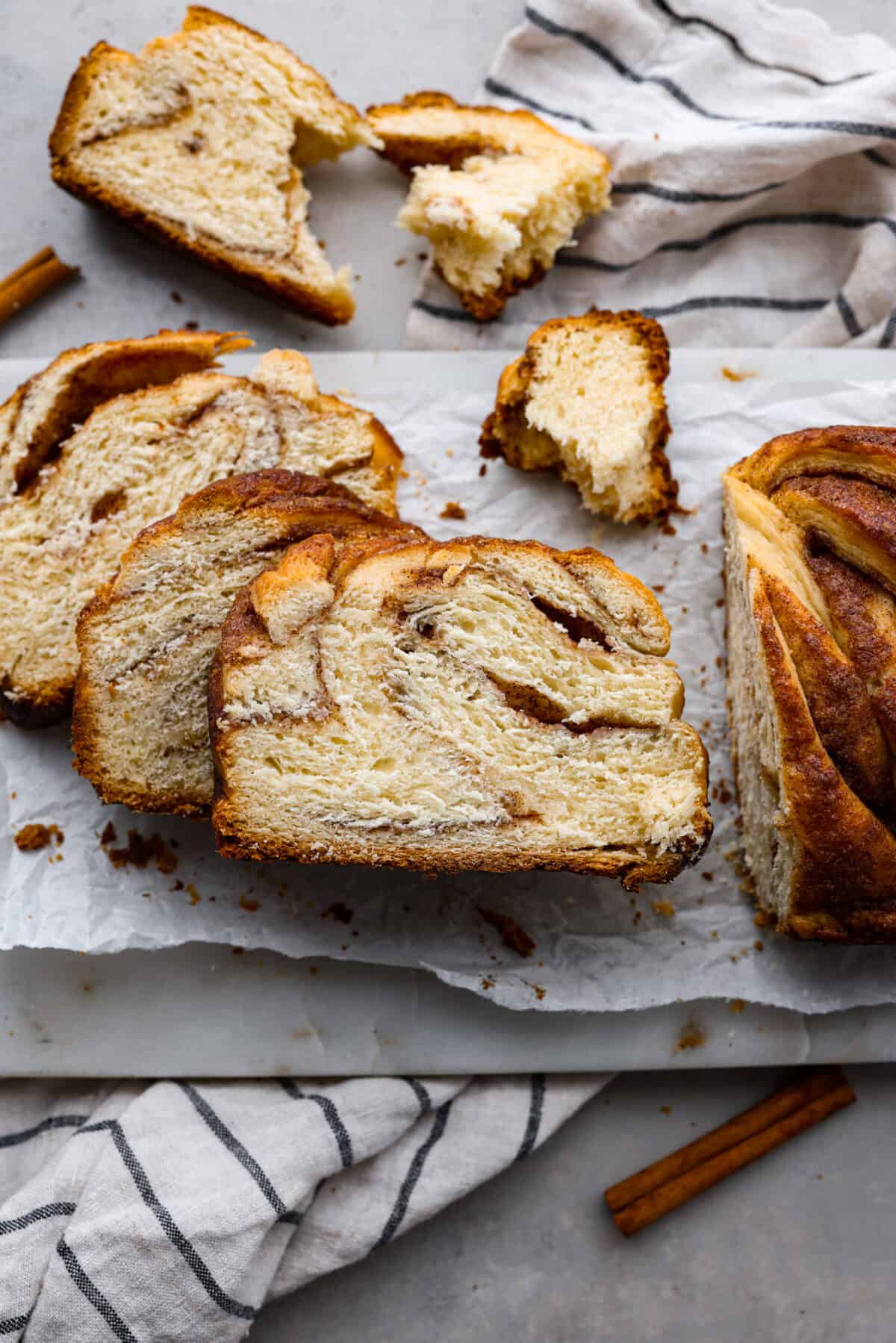 Delicious Cinnamon Babka is rich, buttery bread with swirling ribbons of cinnamon sugar, topped off with aย sweet syrup topping. Tender, soft, and perfectly sweet, this loaf is a welcome treat for any occasion! sliced cinnamon babka bread on parchment paper.