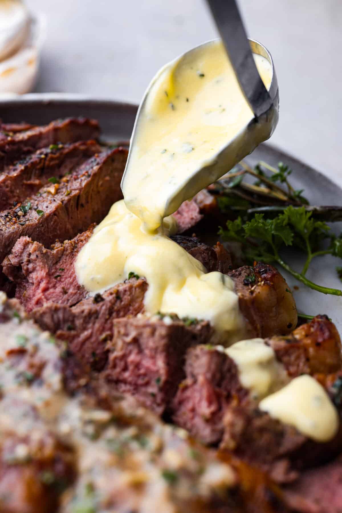 A creamy French steak sauce that you'll want to put on everything! Bearnaise sauce is a tasty variation of hollandaise, infused with shallot, tarragon, and lemon! Pouring sauce over sliced steak.