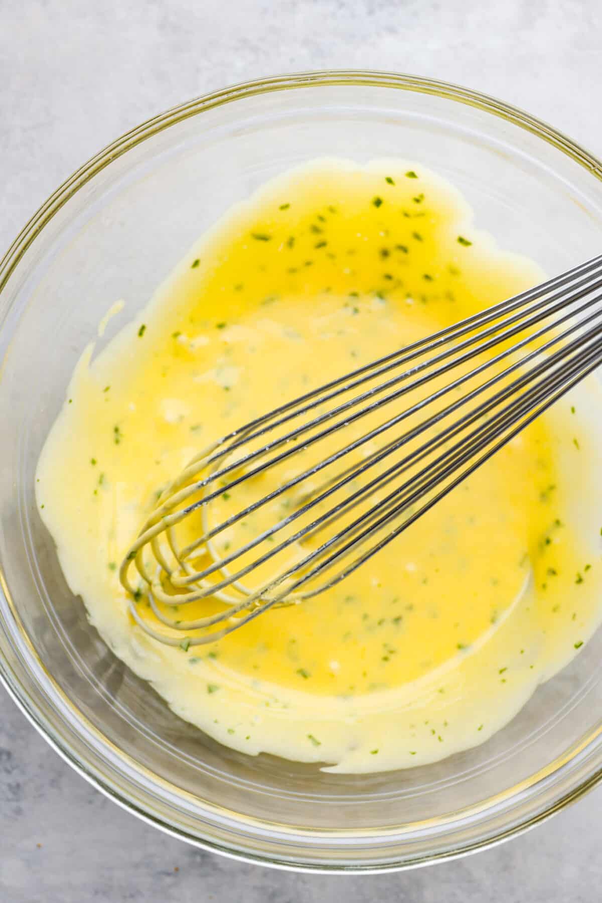 A creamy French steak sauce that you'll want to put on everything! Bearnaise sauce is a tasty variation of hollandaise, infused with shallot, tarragon, and lemon! Bearnaise sauce in a glass bowl, being whisked together.