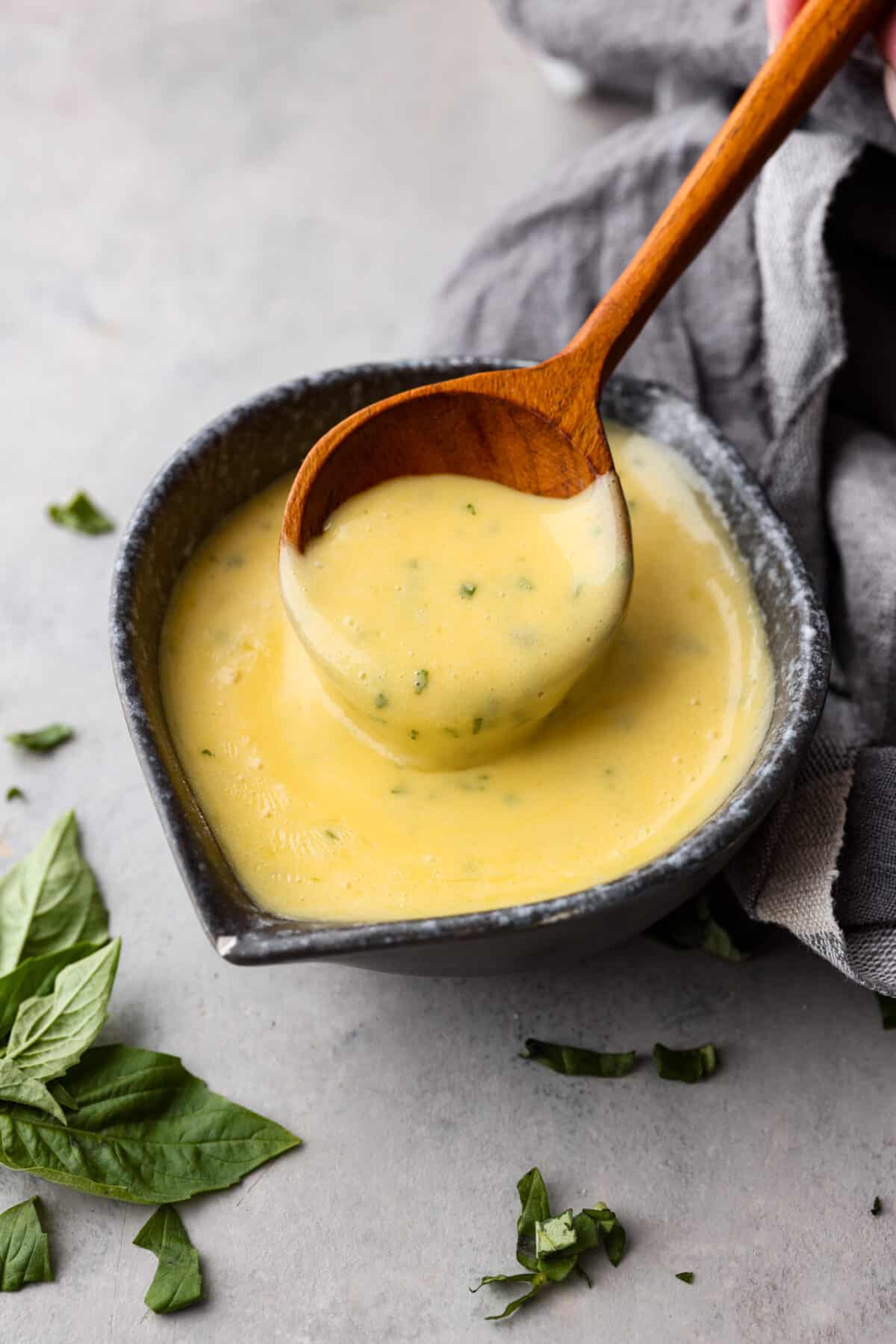 A creamy French steak sauce that you'll want to put on everything! Bearnaise sauce is a tasty variation of hollandaise, infused with shallot, tarragon, and lemon! Bearnaise sauce in a bowl, being scooped up with a wooden spoon.