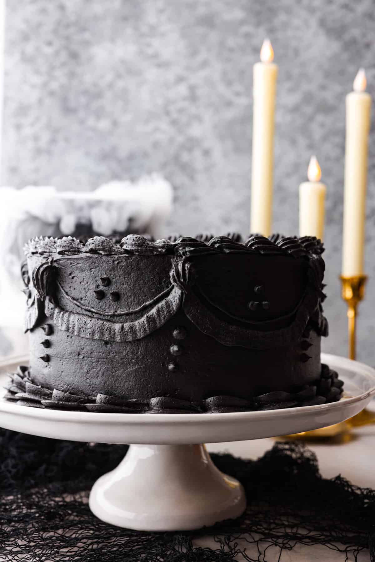 Come to the dark side with this gorgeous black velvet cake! Not only is it a showstopper and perfect for any Halloween party, but supremely moist and delicious to boot! Each bite is loaded with the most amazing cocoa flavor. Hero image of a whole black velvet cake on a serving platter.