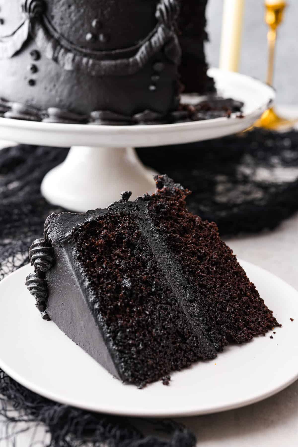 Come to the dark side with this gorgeous black velvet cake! Not only is it a showstopper and perfect for any Halloween party, but supremely moist and delicious to boot! Each bite is loaded with the most amazing cocoa flavor. Closeup of a slice of cake served on a small white plate.