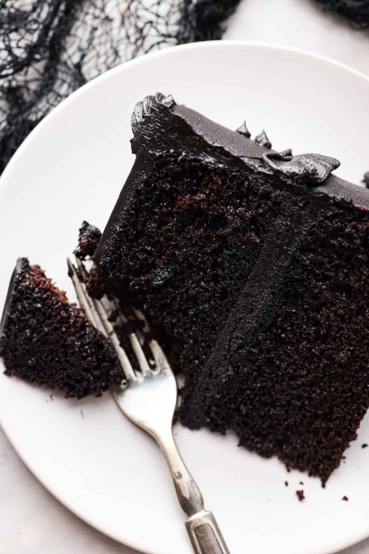 This delicious black frosting is fun to make for special occasions, especially for Halloween, seasonal treats, and desserts. It's made with black cocoa powder, which tastes just like Oreo's! The best part is that it won't dye your mouth, hands, or clothing! It's the perfect frosting for witchy cakes and other dramatic parties. Overhead shot of a plated slice of black velvet cake frosted with black frosting.