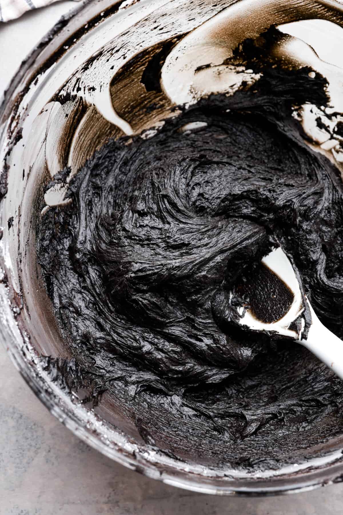 This delicious black frosting is fun to make for special occasions, especially for Halloween, seasonal treats, and desserts. It's made with black cocoa powder, which tastes just like Oreo's! The best part is that it won't dye your mouth, hands, or clothing! It's the perfect frosting for witchy cakes and other dramatic parties. Overhead shot of a bowl of black frosting.