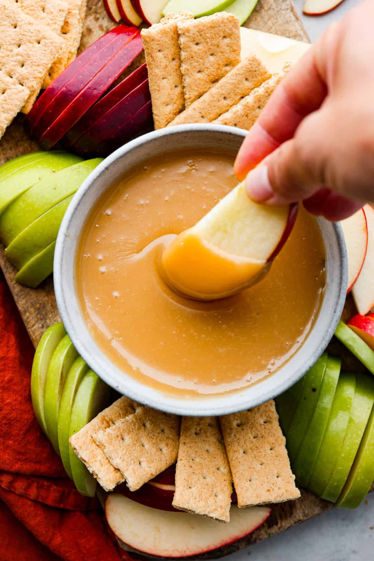 A classic fall treat made into a dip to share! In this caramel apple dip recipe, butter, caramels, and condensed milk get melted together to create the most indulgent treat. It's heavenly! Hero image of an apple slice being dipped in caramel.