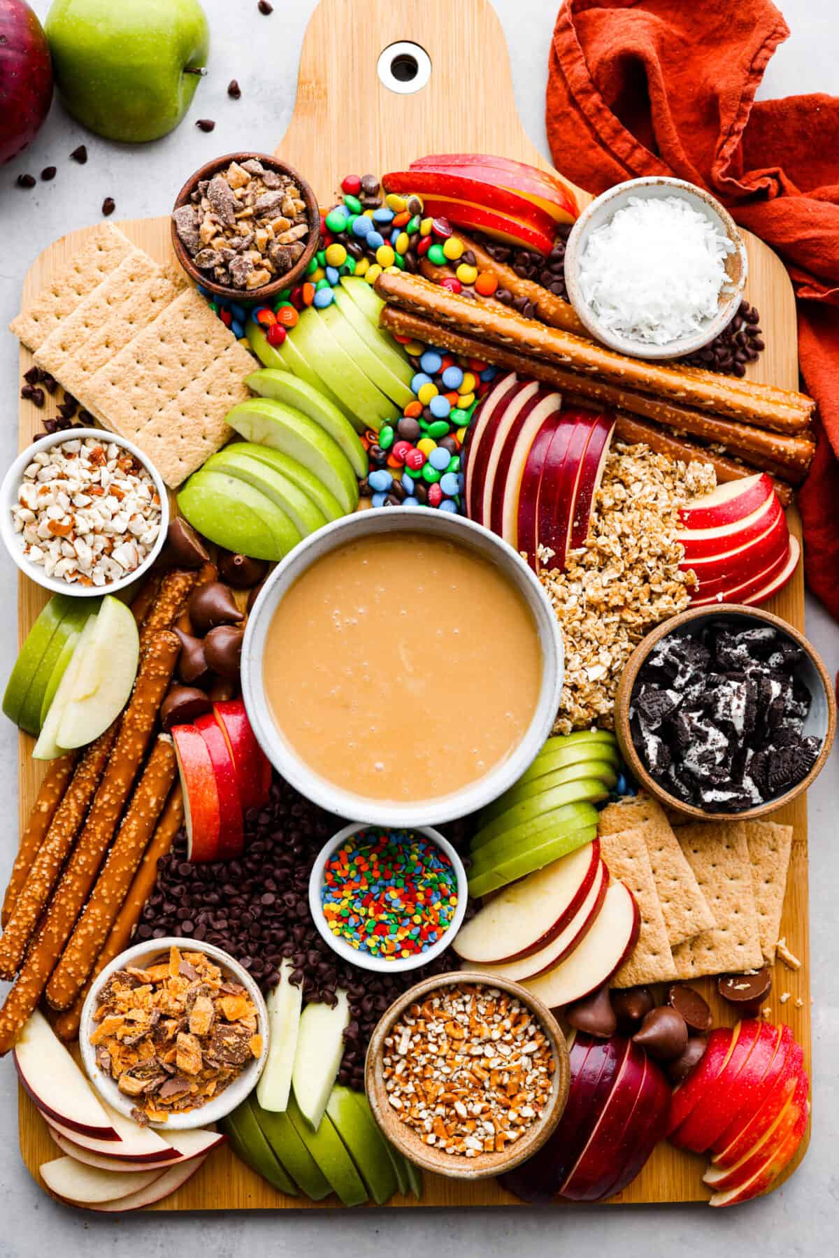 Everybody loves a good caramel apple, especially when they can customize it just the way they like! Make this caramel apple charcuterie board for your next fall party, I promise it will be a huge hit! It has a fun variety of toppings and things for dipping, so thereโs something for everyone! Top-down view of a whole caramel apple charcuterie board, filled with various cookies, candy, pretzels, crackers, and apple slices.