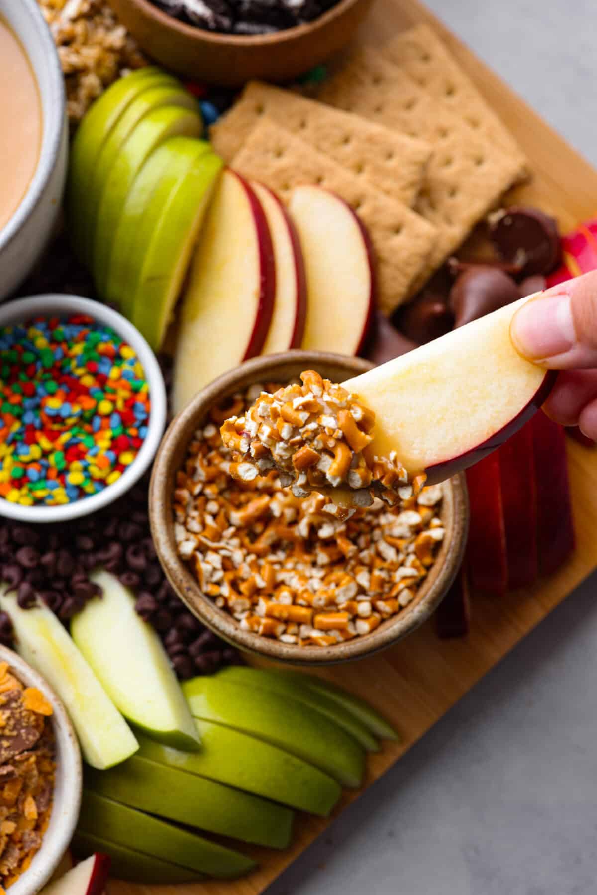 Everybody loves a good caramel apple, especially when they can customize it just the way they like! Make this caramel apple charcuterie board for your next fall party, I promise it will be a huge hit! It has a fun variety of toppings and things for dipping, so thereโs something for everyone! A caramel apple slice that has been dipped in caramel and then crushed pretzels.