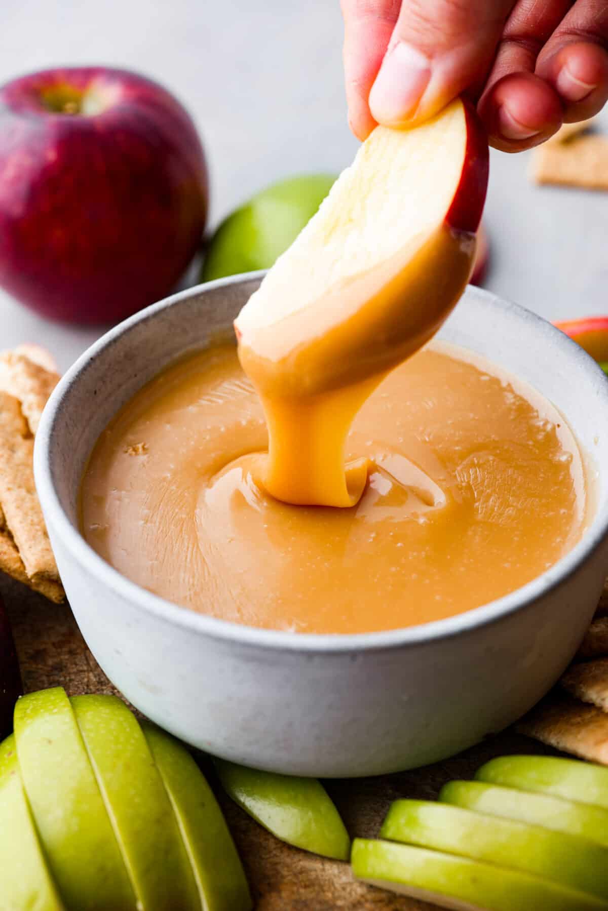 A classic fall treat made into a dip to share! In this caramel apple dip recipe, butter, caramels, and condensed milk get melted together to create the most indulgent treat. It's heavenly! Closeup of caramel apple dip and an apple slice.