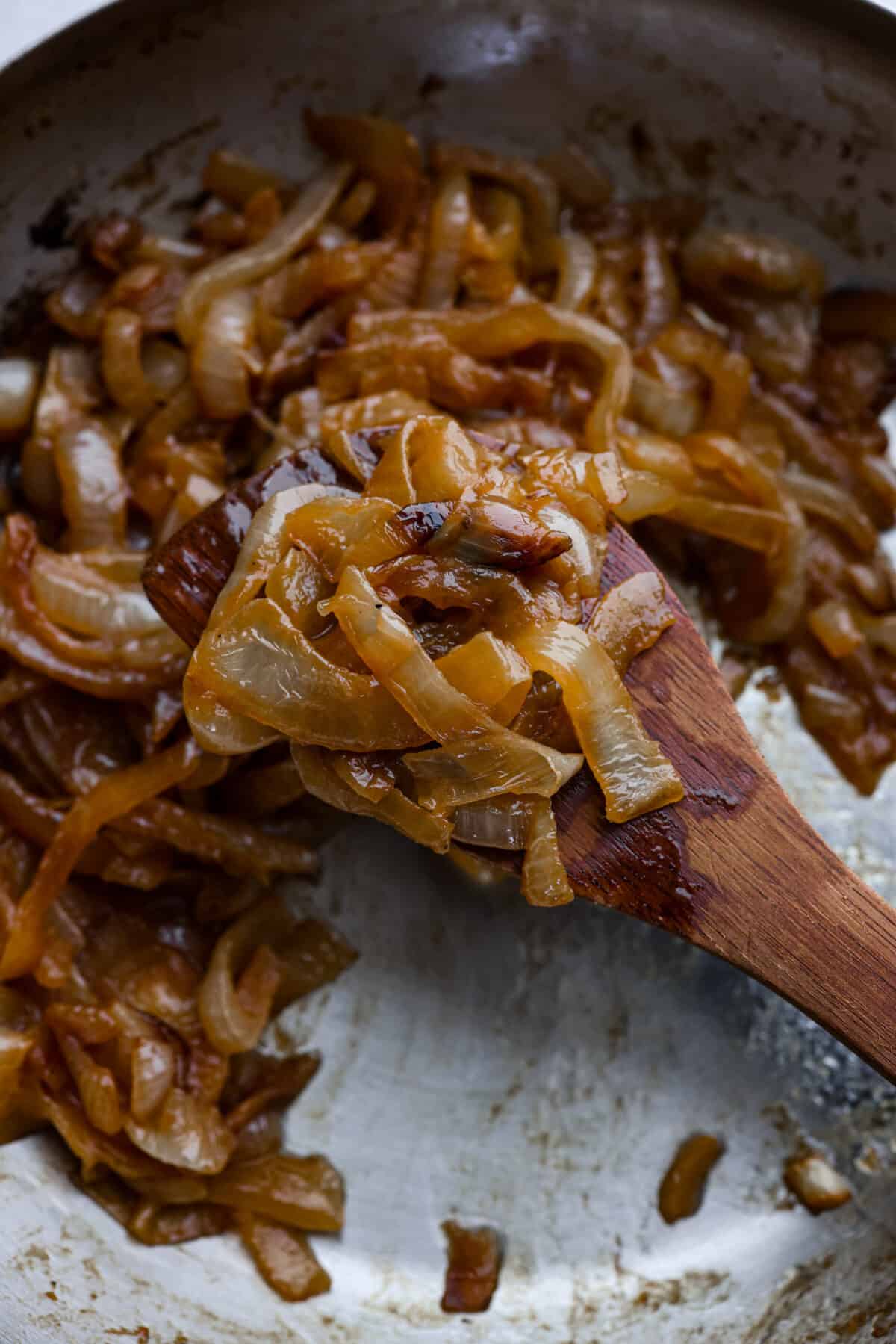 Knowing how to make caramelized onions is one of the best kitchen skills for a home chef to learn! Onions, salted butter and water is all you need to have the most rich, sweet and savory ingredient to bring complex flavor to everything from pizza and pasta to burgers and fajitas. Closeup of caramelized onions on a wooden spoon.