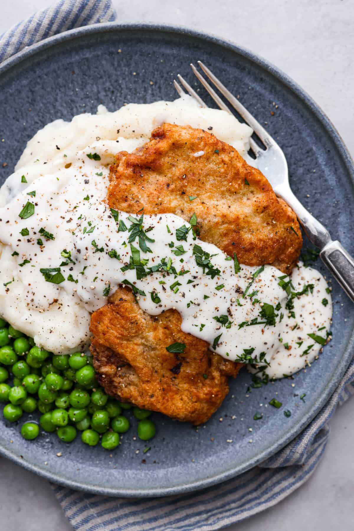 Chicken Fried Steak. The ultimate in Southern comfort food! Tender seasoned steak, coated in a thick batter and fried until golden brown with a creamy gravy drizzled on top. Simple, basic ingredients are all that is needed to bring this recipe to life in your own kitchen! A chicken fried steak served with mashed potatoes, cream gravy, and peas.