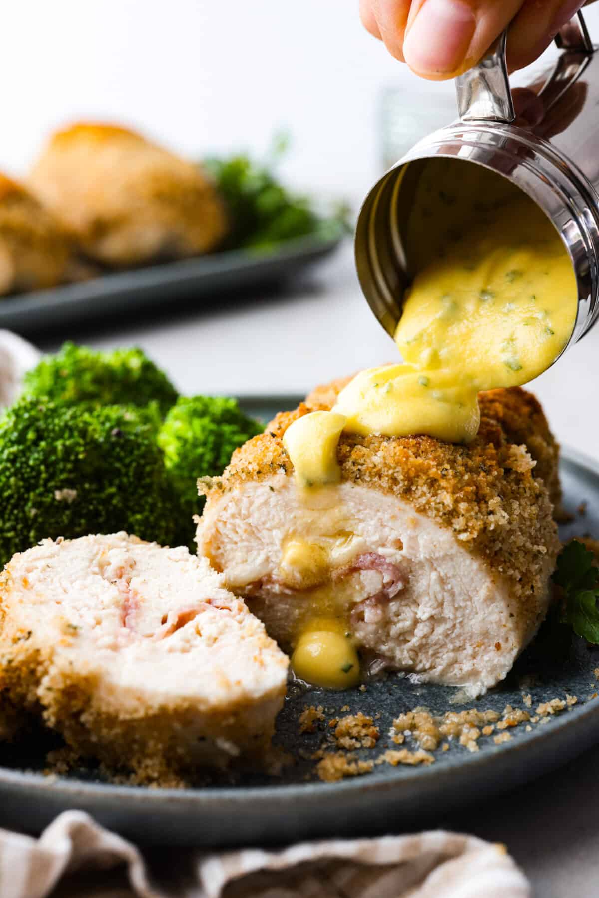 Chicken cordon bleu has a delicious layer of ham and cheese wrapped inside succulent crumb-coated chicken breast. Drizzled with mustard cream sauce, this oven-baked chicken is a classic French recipe your family will love! Close side view of chicken cordon bleu sliced and drizzled with sauce.