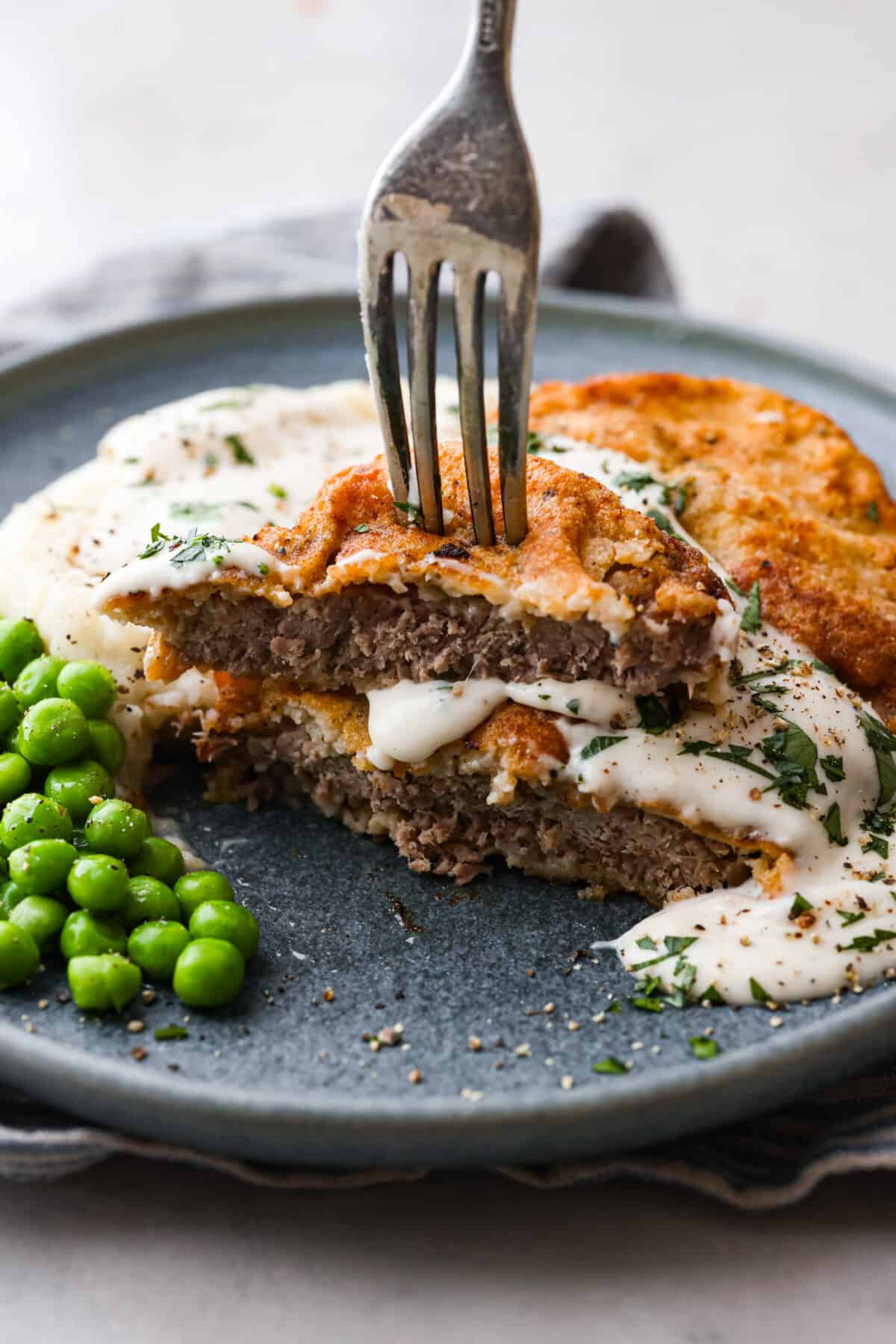 Chicken Fried Steak. The ultimate in Southern comfort food! Tender seasoned steak, coated in a thick batter and fried until golden brown with a creamy gravy drizzled on top. Simple, basic ingredients are all that is needed to bring this recipe to life in your own kitchen! A chicken fried steak that has been cut in half.