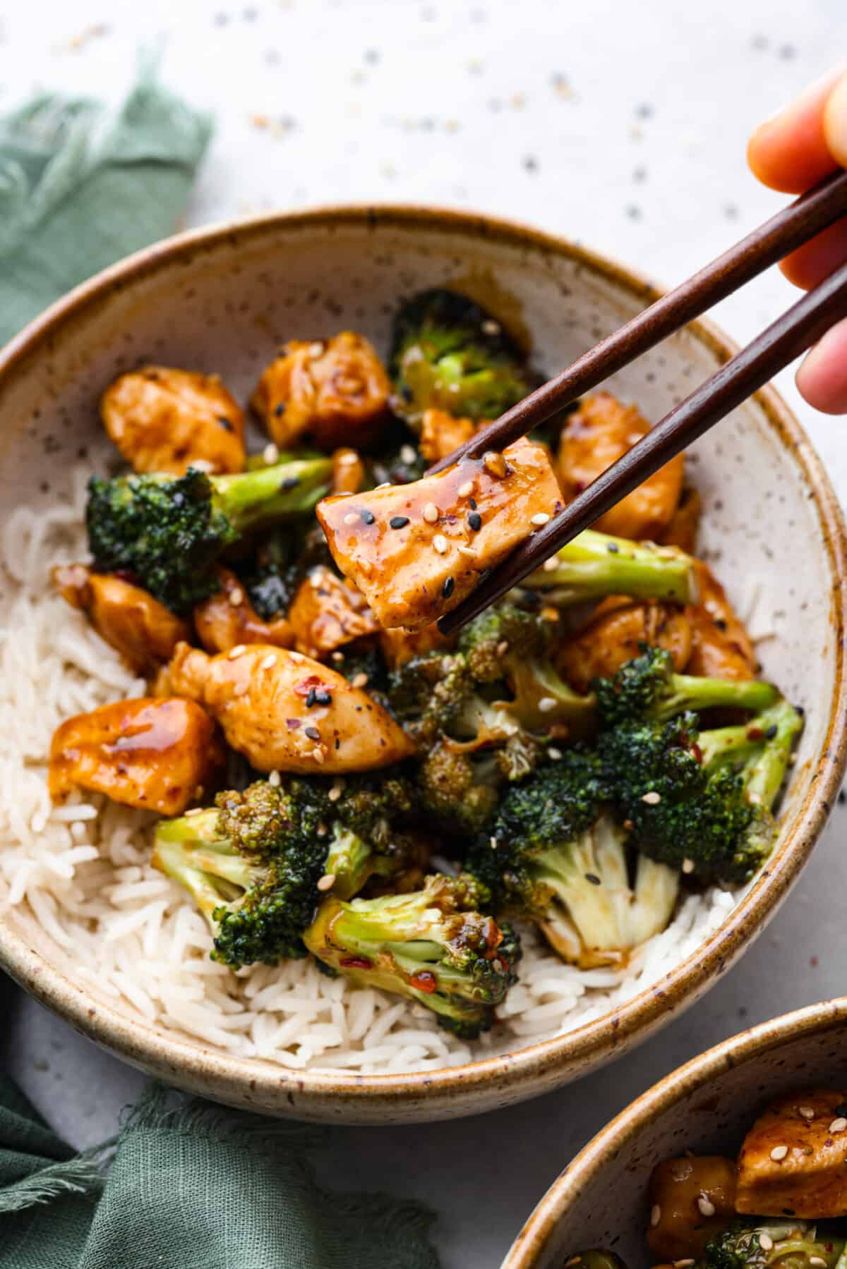 This flavorful Chinese Chicken and Broccoli dish is made in just one pan and is ready in less than 30 minutes!ย Small pieces of tender chicken and broccoli florets are cooked in an irresistible sweet and savory sauce. Serve over rice with a sprinkle of sesame seeds and red pepper flakes for an amazing meal! Picking up a piece of chicken with chopsticks.