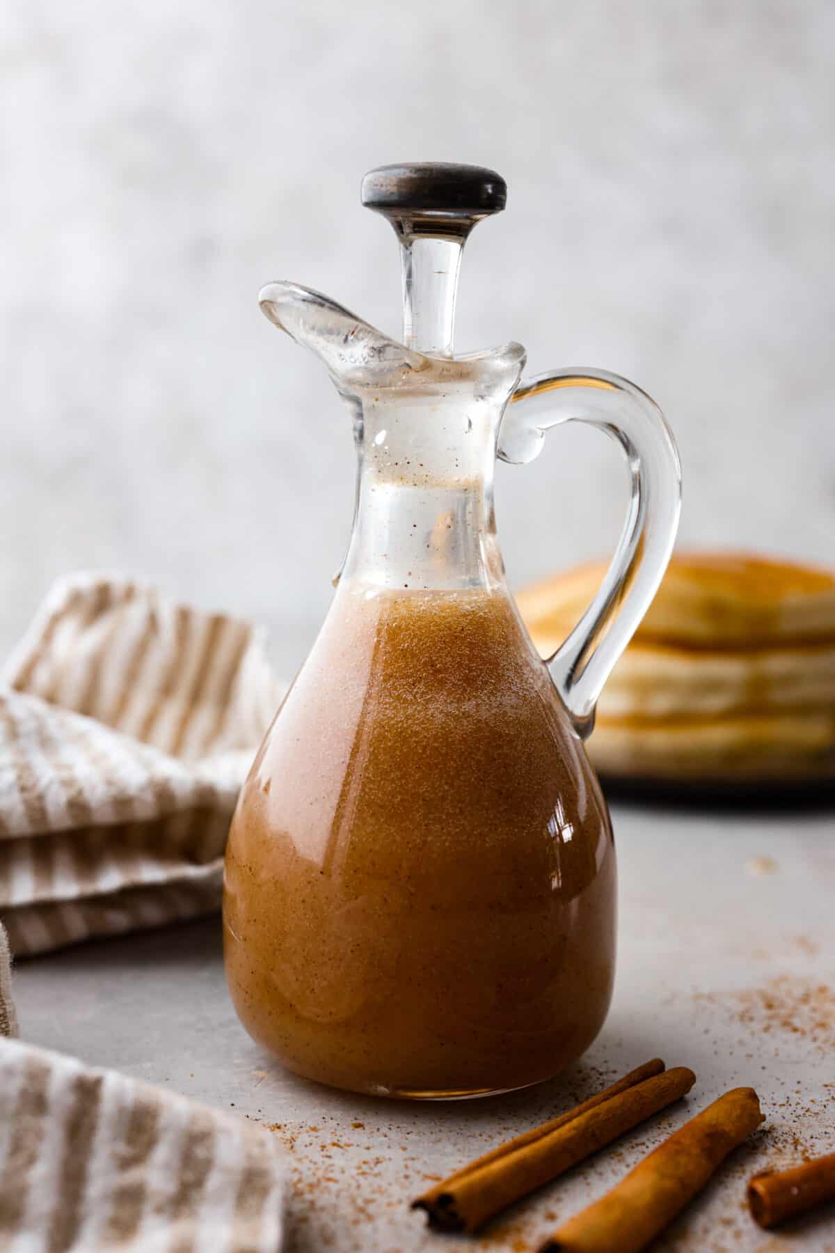 Cinnamon Syrup is the best way to take your pancakes to the next level! It's creamy and buttery and adds delicious cinnamon roll flavor to pancakes, waffles, or anything else you want to sweeten up! Side shot of cinnamon syrup in small glass container.