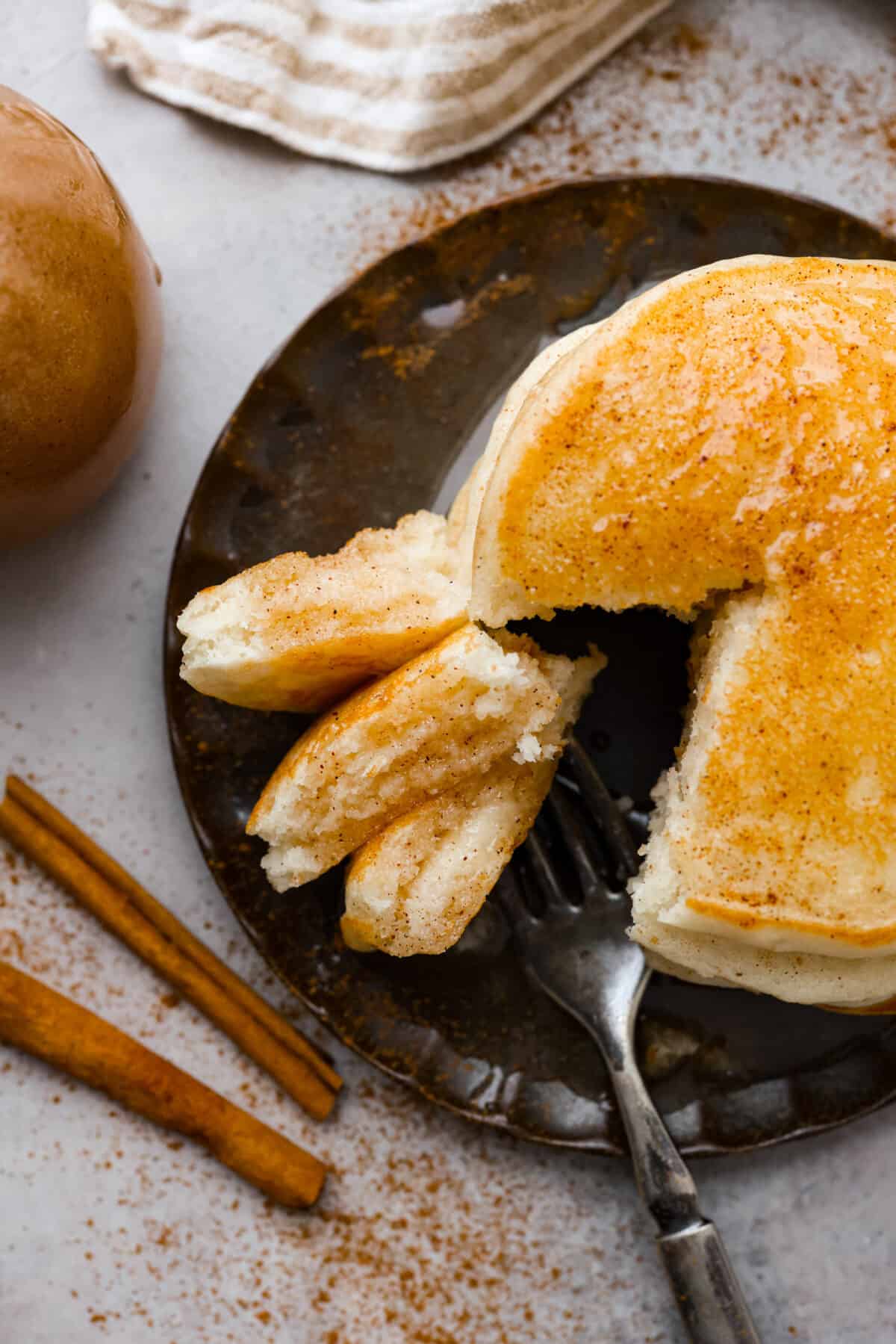 Cinnamon Syrup is the best way to take your pancakes to the next level! It's creamy and buttery and adds delicious cinnamon roll flavor to pancakes, waffles, or anything else you want to sweeten up! Overhead shot of plated pancakes with a bit taken out.