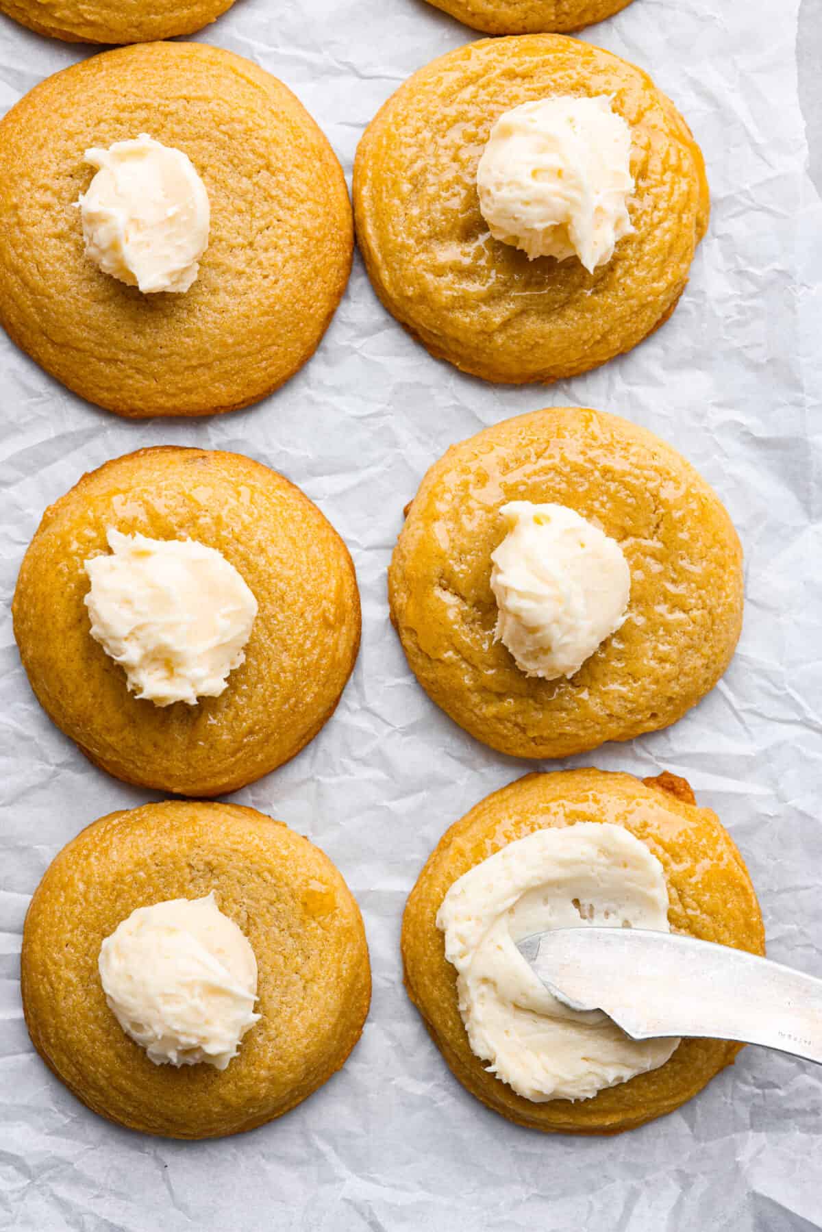 Sweet and buttery cornbread cookies are my favorite cookie Crumbl makes, and I knew I had to recreate this dream cookie. The texture of the cornmeal, the honey butter frosting, and the honey drizzled on top... it all melts in your mouth! Top view of cornbread cookies with a dollop of frosting on top of each cookie. A knife is spreading the frosting on one of the cookies.