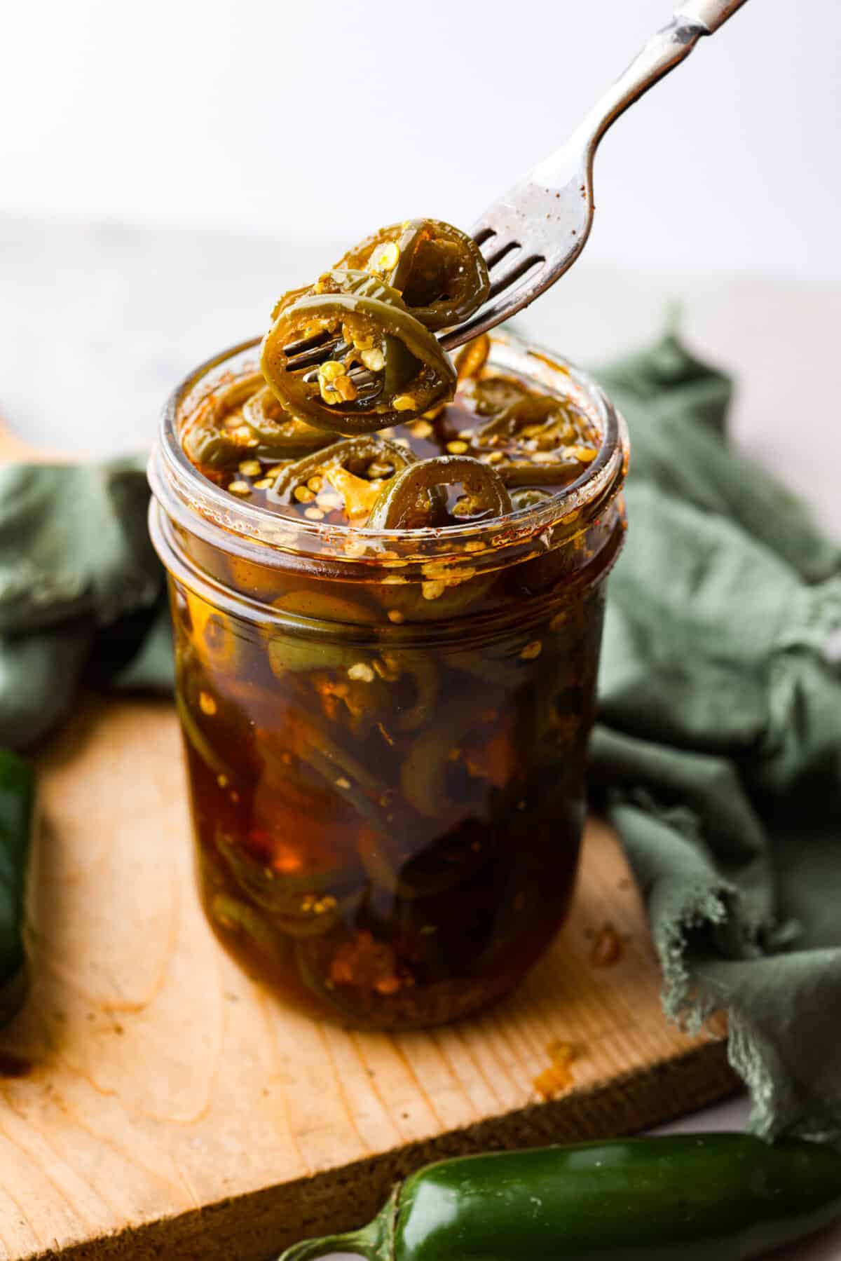 Cowboy candy is a spicy and sweet condiment made from jalapeรฑo peppers. The jalapeรฑos are sliced and simmered in a mix of sugars, vinegar, and spices until they're glossy and deliciously zesty. They're the perfect addition to burgers, sandwiches, hot dogs, you name it! Picking up a candied jalapeno with a fork.