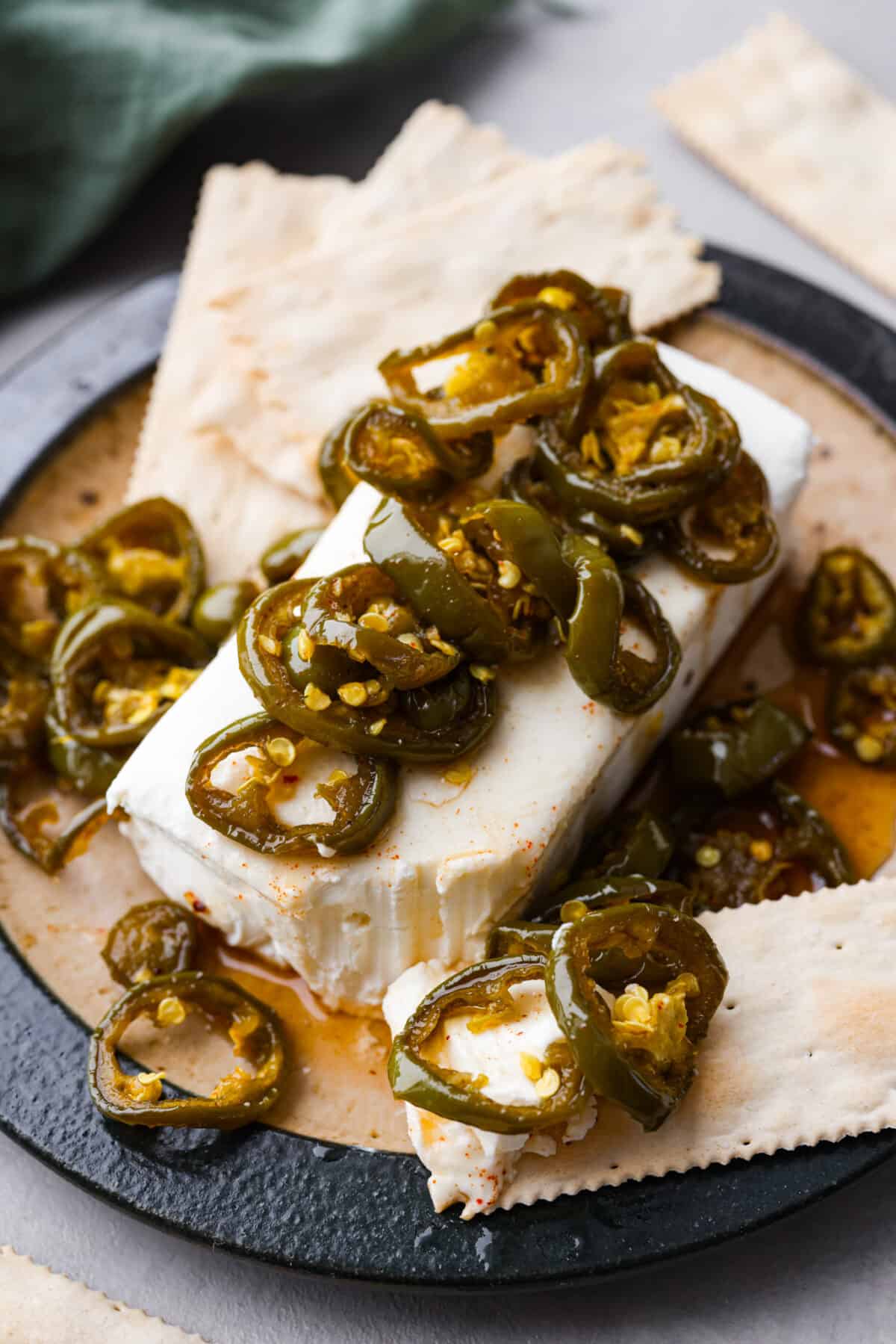 Cowboy candy is a spicy and sweet condiment made from jalapeรฑo peppers. The jalapeรฑos are sliced and simmered in a mix of sugars, vinegar, and spices until they're glossy and deliciously zesty. They're the perfect addition to burgers, sandwiches, hot dogs, you name it! A block of cheese topped with cowboy candy, served with crackers.