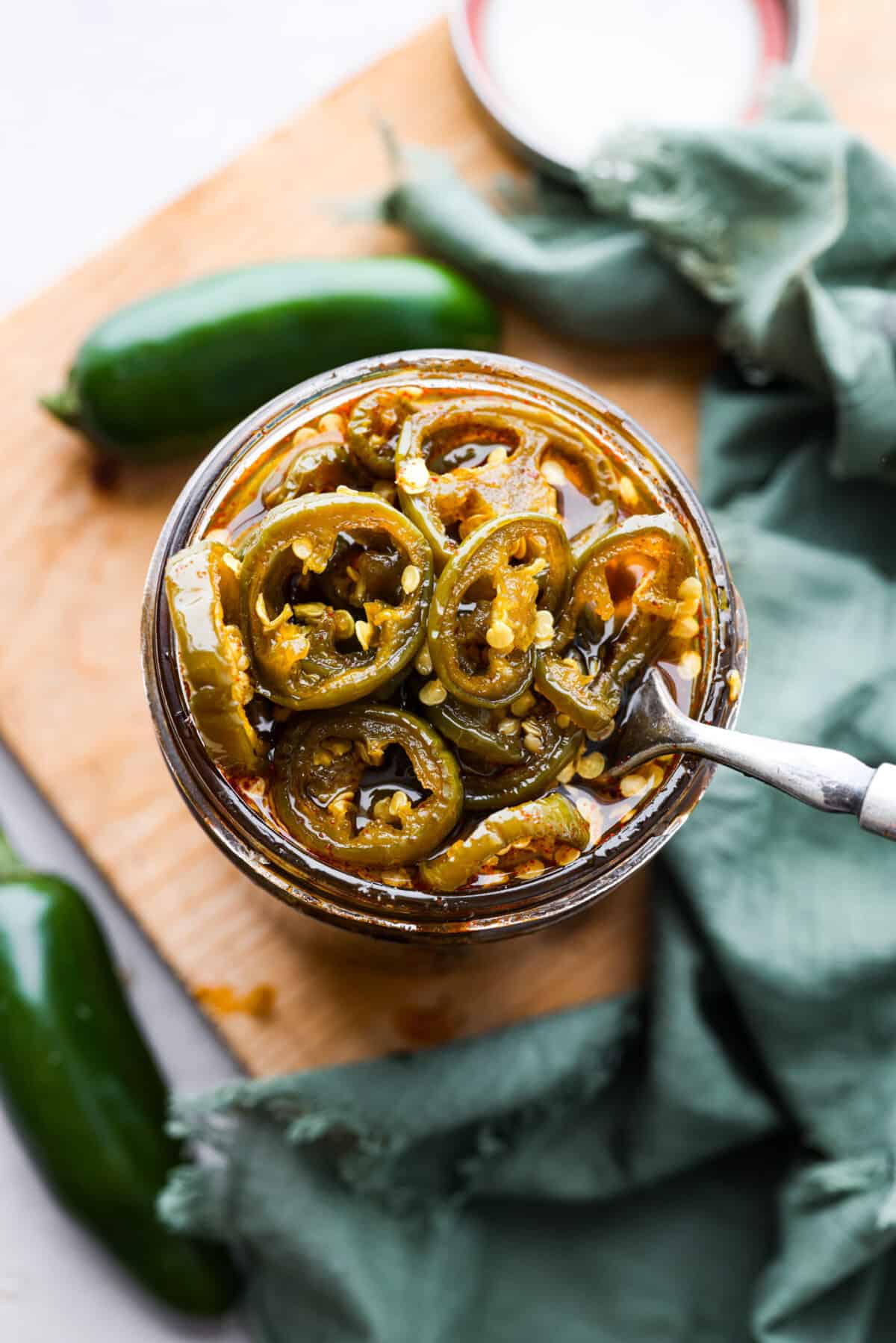 Cowboy candy is a spicy and sweet condiment made from jalapeรฑo peppers. The jalapeรฑos are sliced and simmered in a mix of sugars, vinegar, and spices until they're glossy and deliciously zesty. They're the perfect addition to burgers, sandwiches, hot dogs, you name it! Top-down view of a jar of cowboy candy.