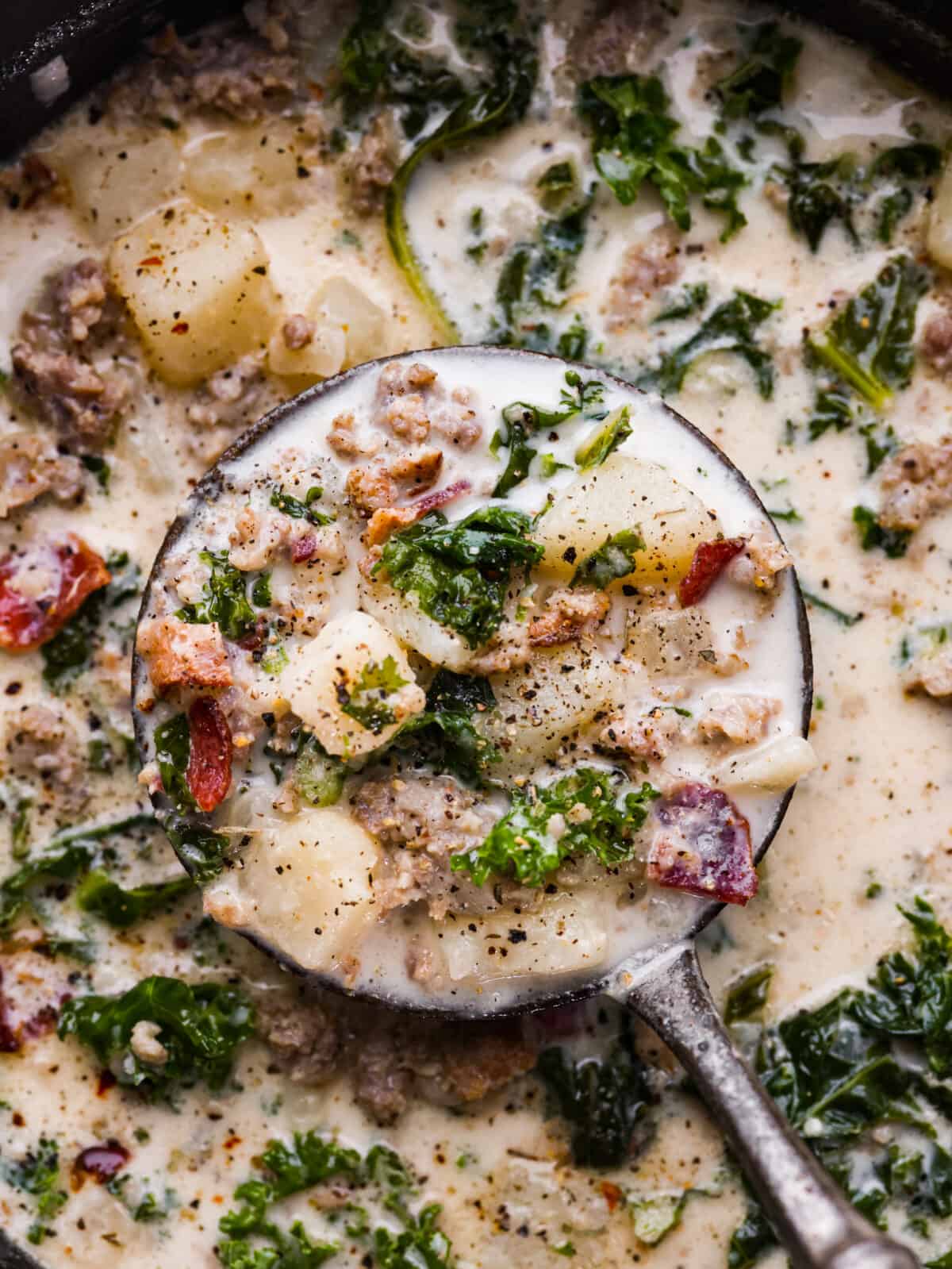 Creamy Zuppa Toscana is a savory Italian soup that is made with potatoes, spicy sausage, bacon, and kale. It is thick, creamy, and delicious and is a must-make soup this fall! A close up of Zuppa Toscana in a ladel.
