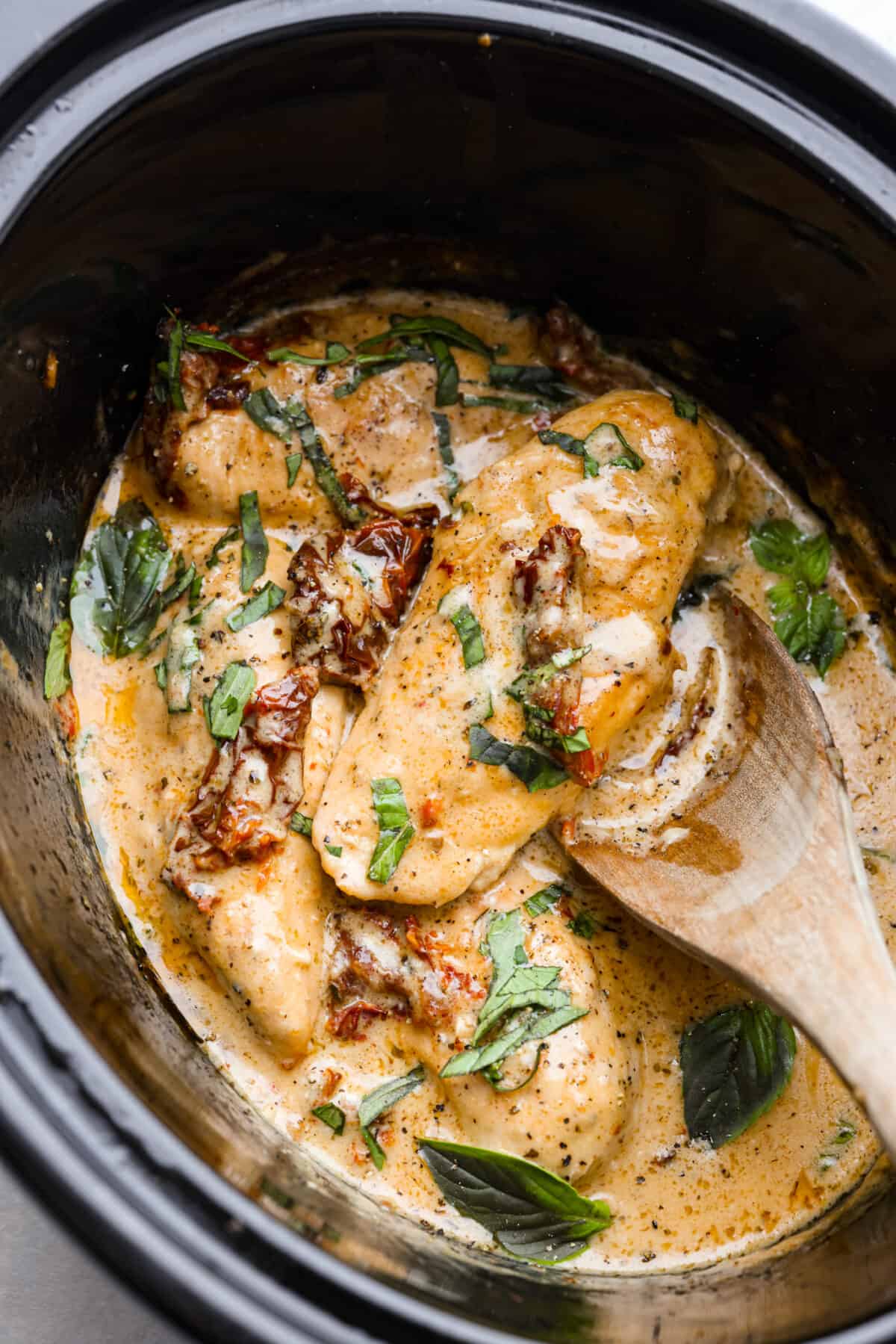 An amazing Tuscan dish made easy in the slow cooker! This Crock Pot Marry Me Chicken is slow cooked to tender perfection and smothered in a creamy, savory sauce made with sun-dried tomatoes and parmesan cheese. The perfect way to win anyone over! Cooked Tuscan chicken in a crock pot, garnished with fresh basil.
