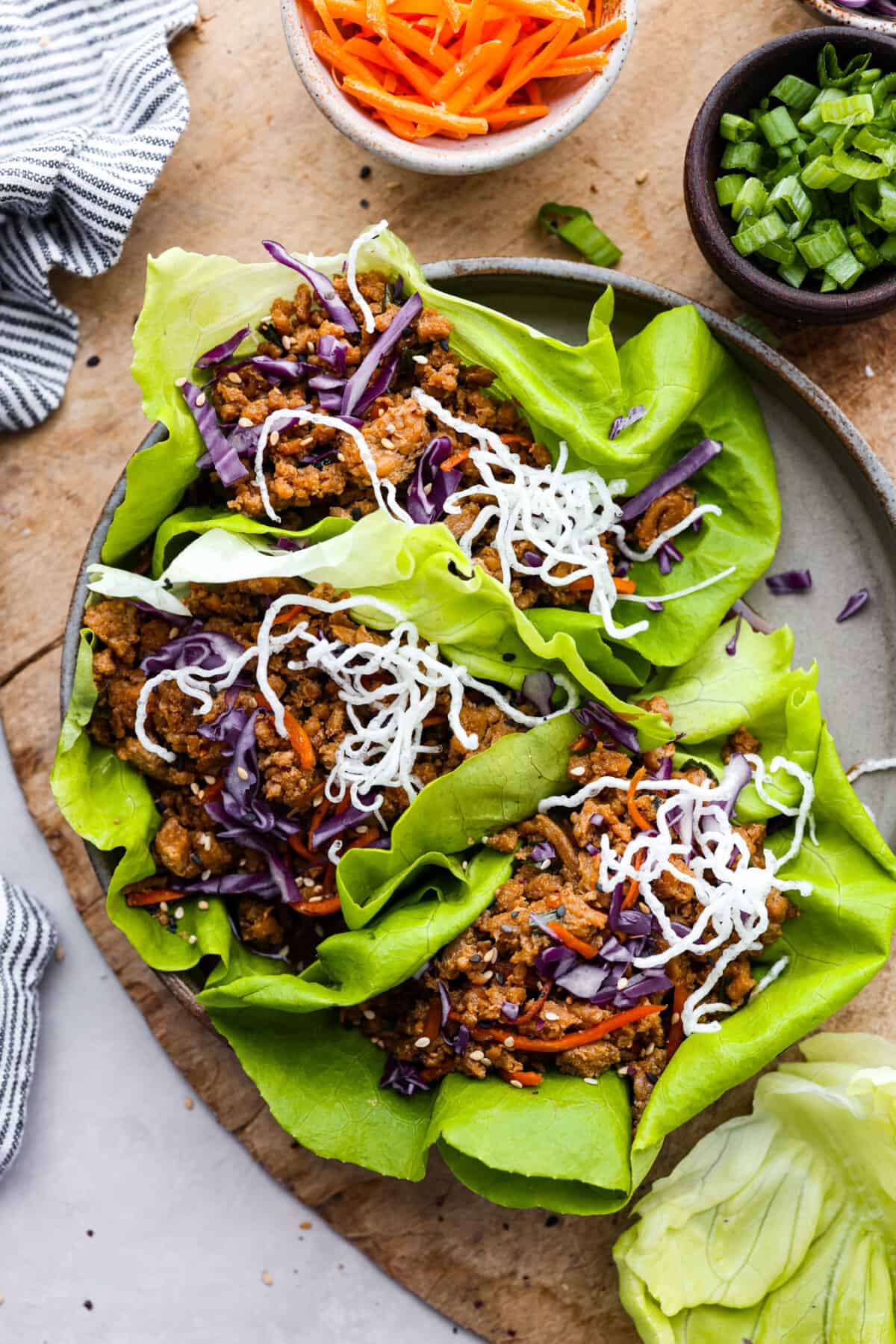 Healthy and easy, these Chicken Lettuce Wraps are so fresh and delicious! They're ready in under 30 minutes with a juicy chicken filling and crispy butterhead lettuce. Top-down view of lettuce wraps on a gray plate.