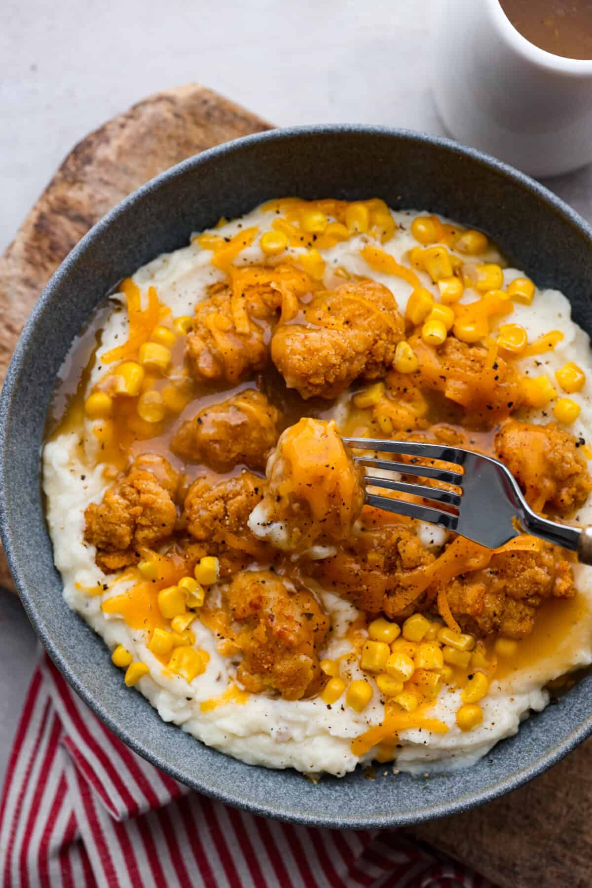 This irresistible copycat KFC Famous Bowl is super quick and easy to make at home and tastes even better than the fast food classic. It's a warm & comforting dinner that the whole family will enjoy! Crispy chicken, mashed potatoes and gravy and corn served in a gray bowl.