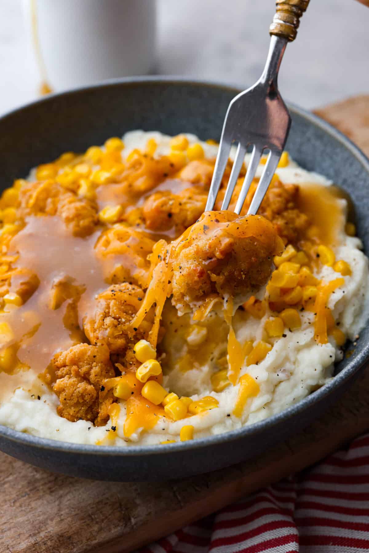 This irresistible copycat KFC Famous Bowl is super quick and easy to make at home and tastes even better than the fast food classic. It's a warm & comforting dinner that the whole family will enjoy! Taking a bite of a KFC Famous Bowl.